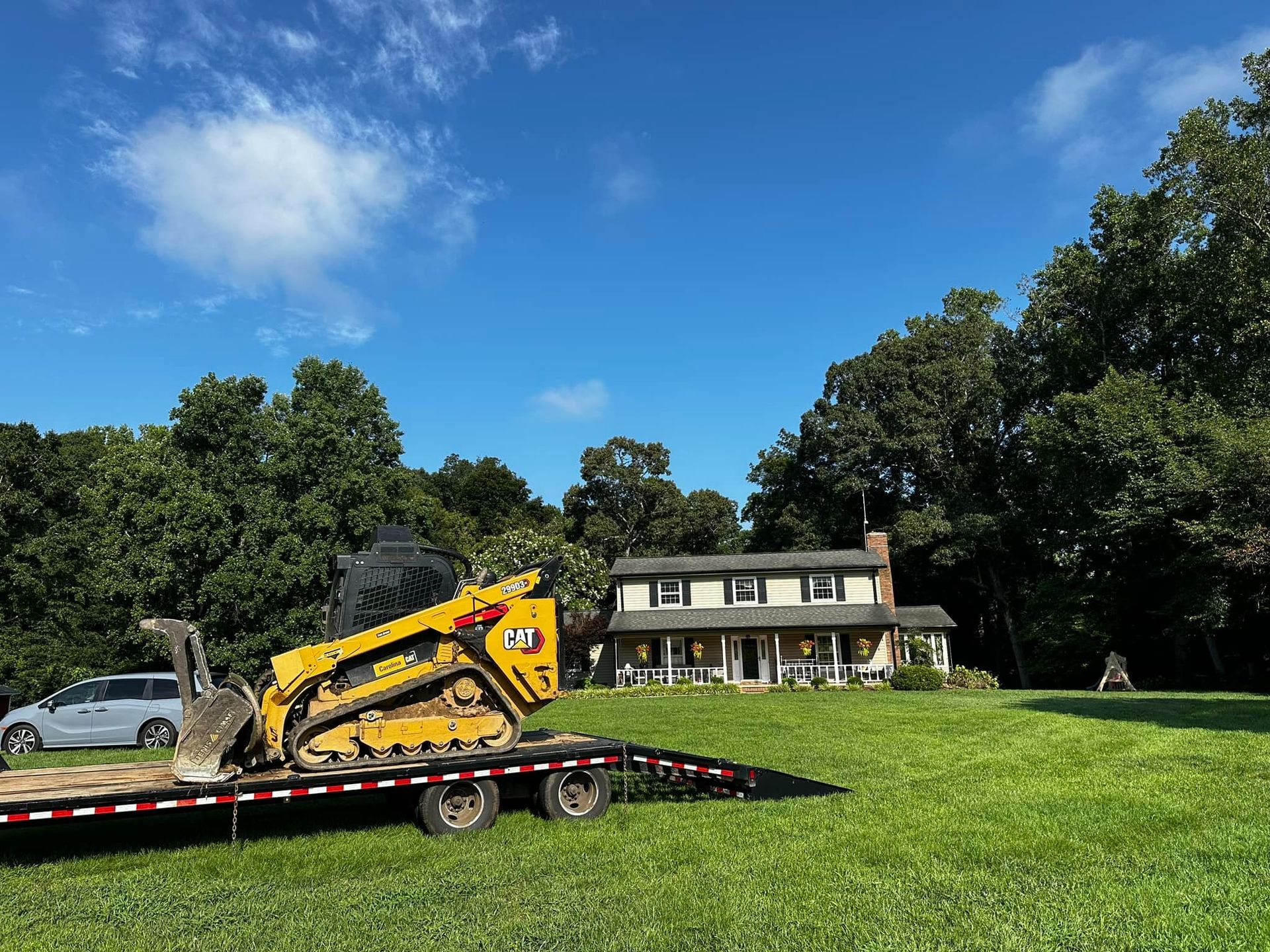 A bulldozer is on a trailer in front of a house.