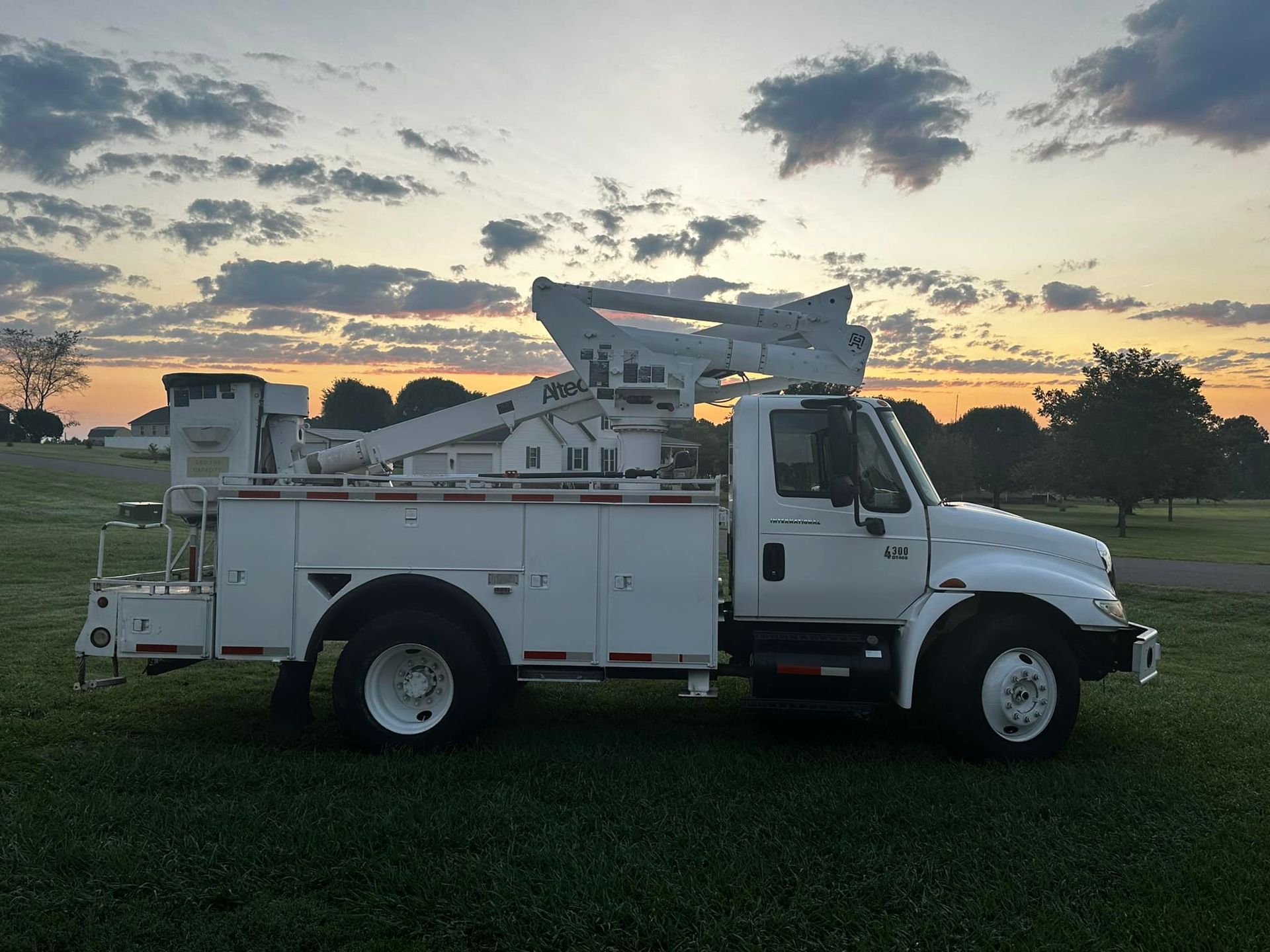 A white utility truck is parked in a grassy field at sunset.
