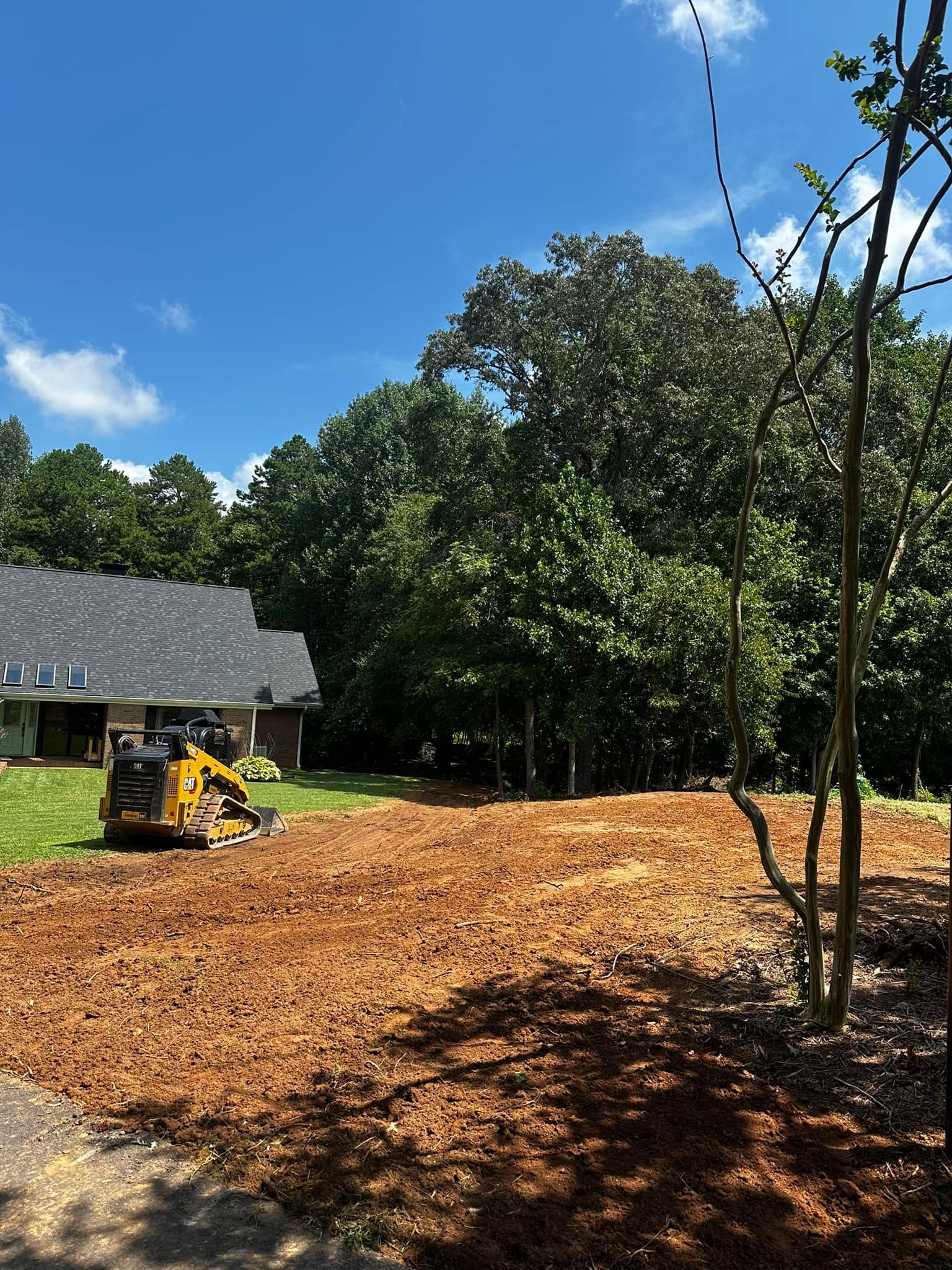 A stump grinder is sitting in a dirt field in front of a house.
