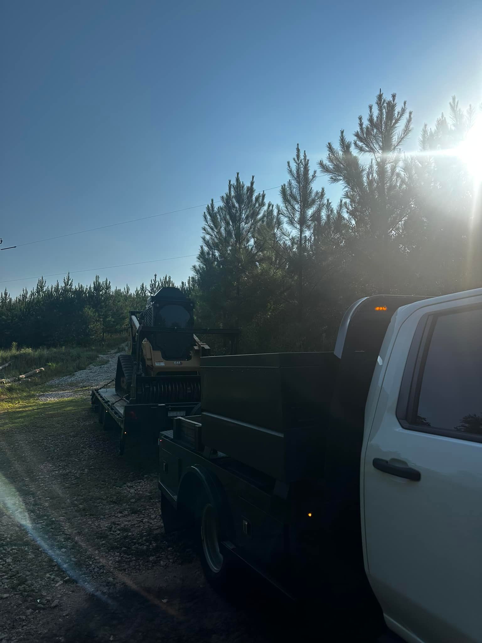 A white truck is parked next to a black truck with a trailer attached to it.