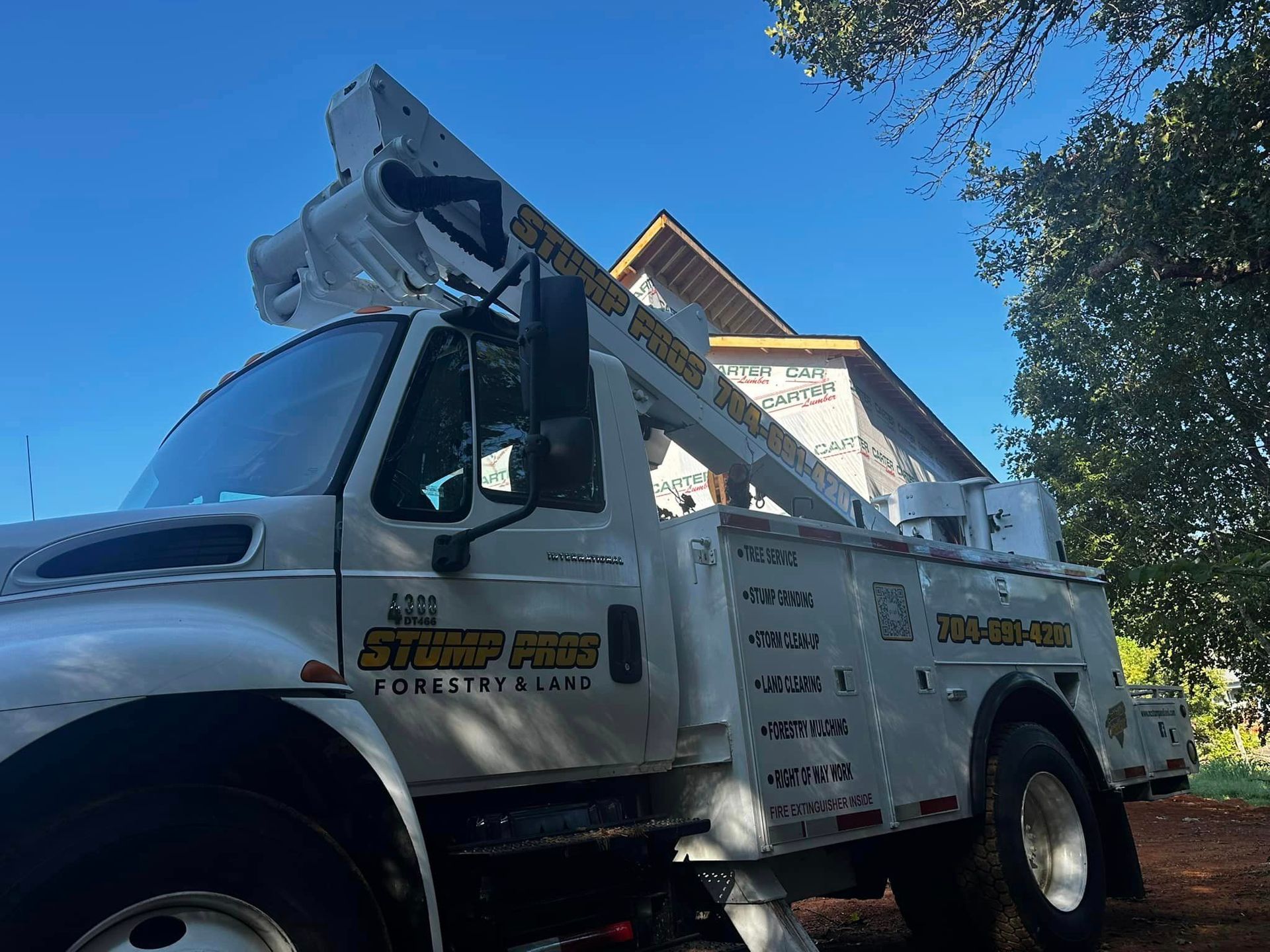 A white truck with a crane on the back is parked in front of a house.