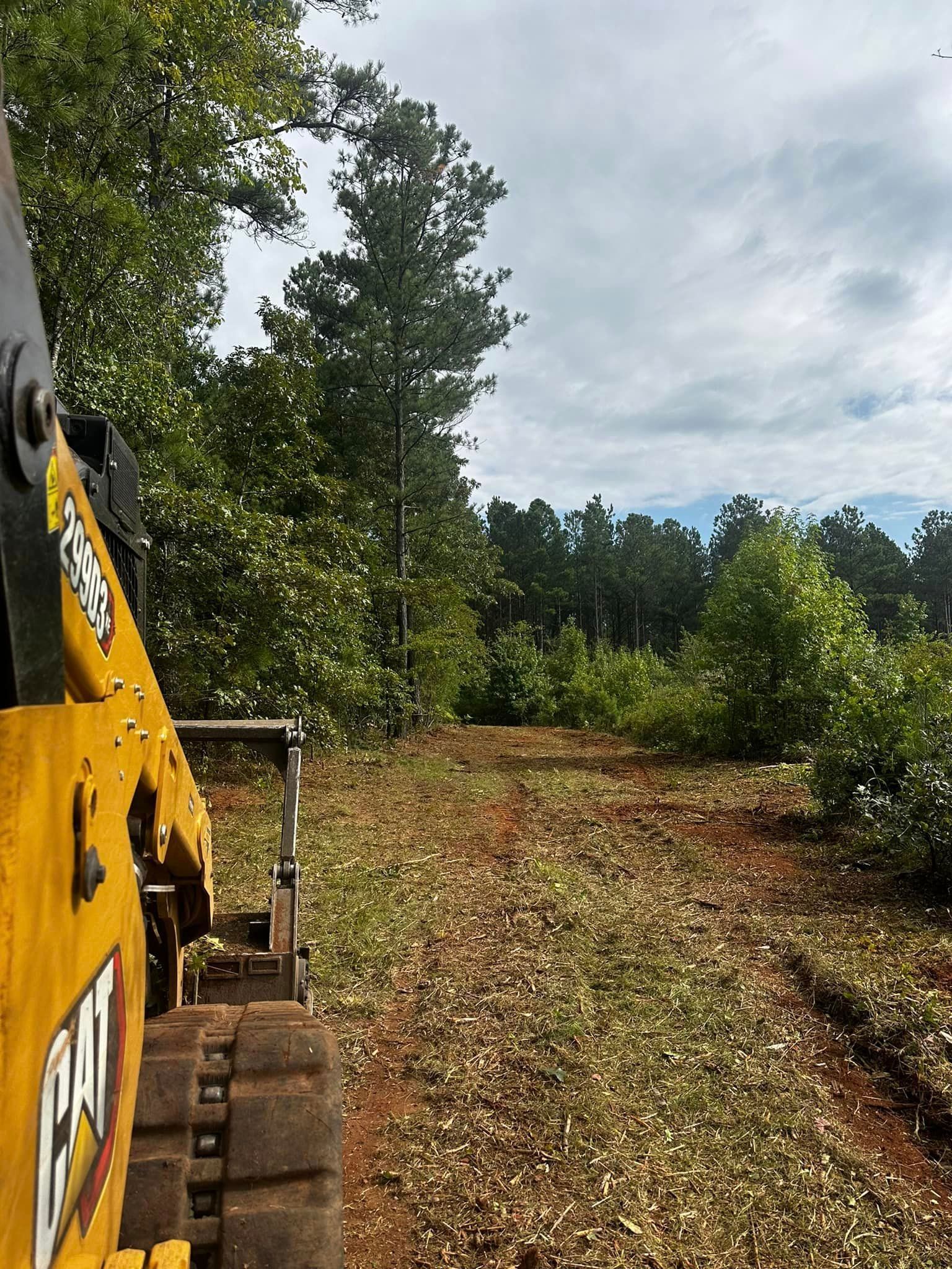 A yellow bulldozer is driving down a dirt road in the woods.