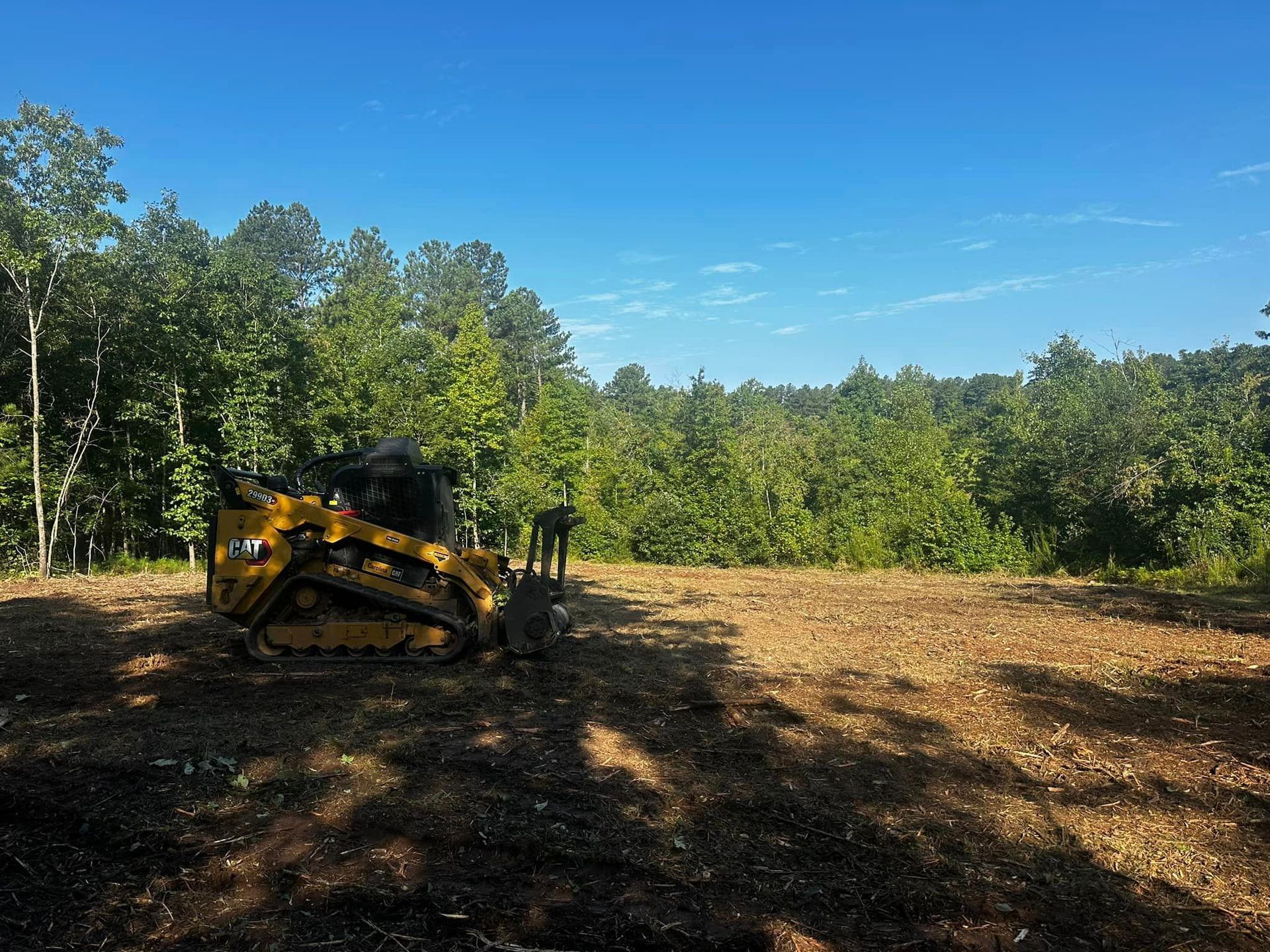 A yellow bulldozer is sitting in a field with trees in the background.