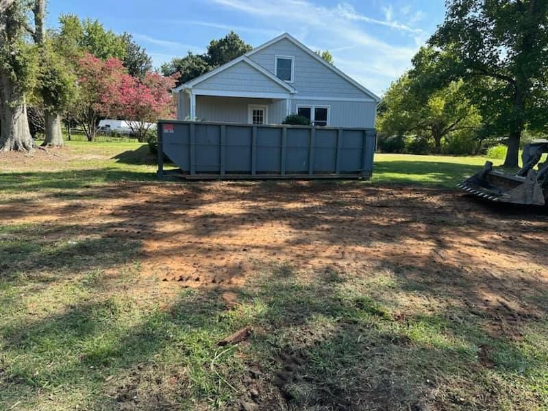 A dumpster is sitting in the grass in front of a house.