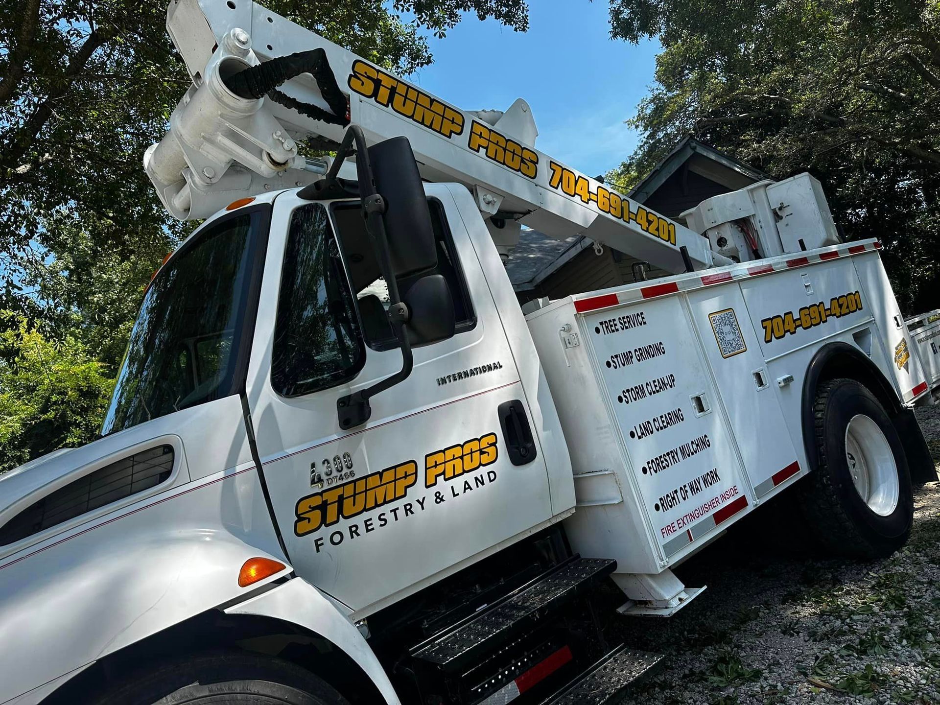 A white stump removal truck is parked in front of a house.