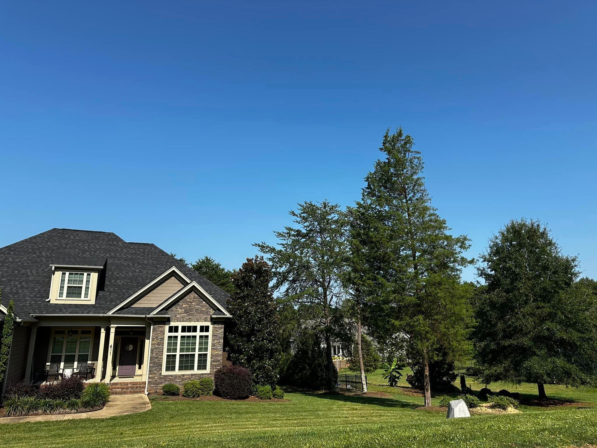 A house with a black roof is sitting in the middle of a lush green field.
