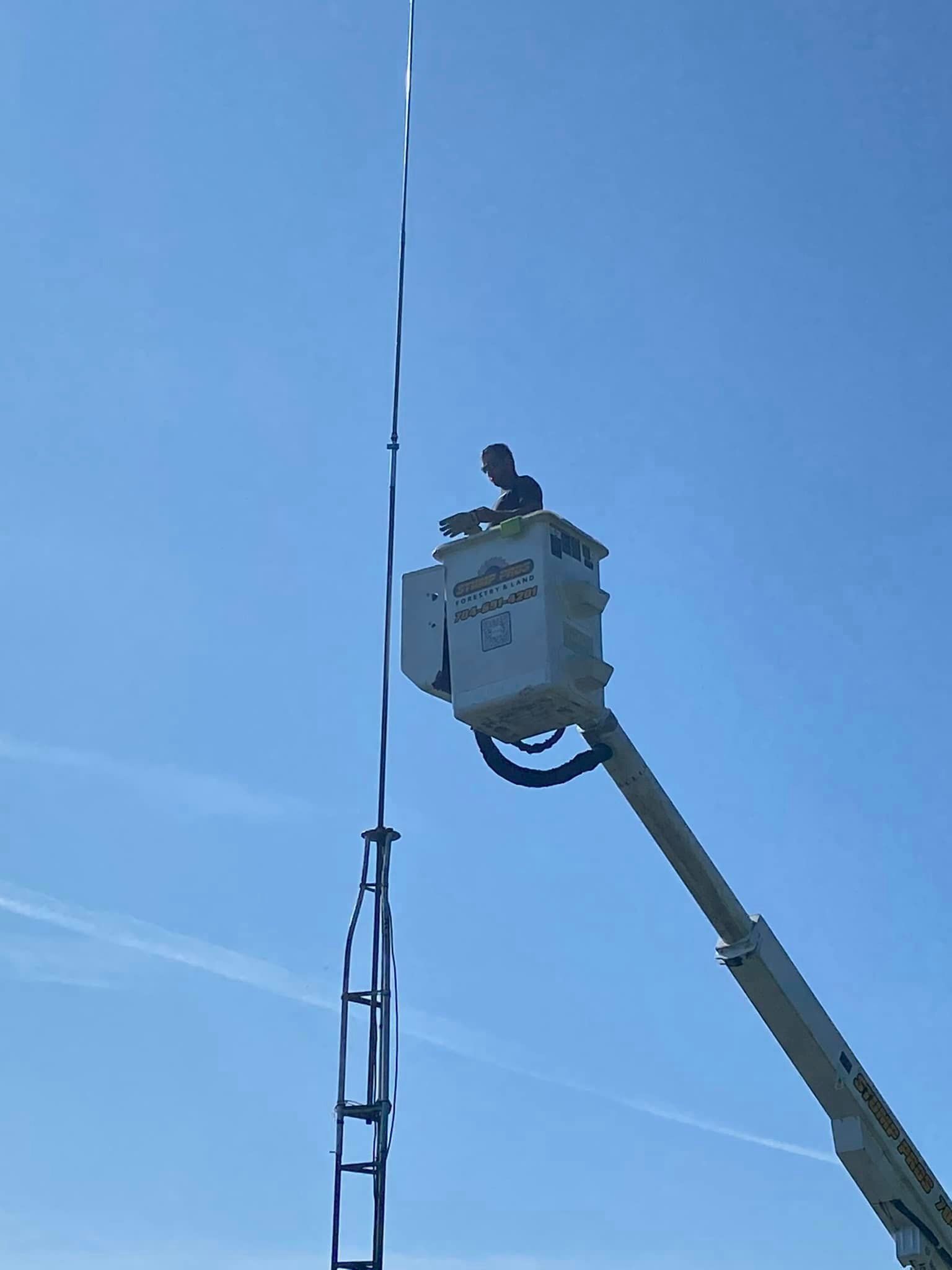 A man is sitting in a bucket on top of a crane.