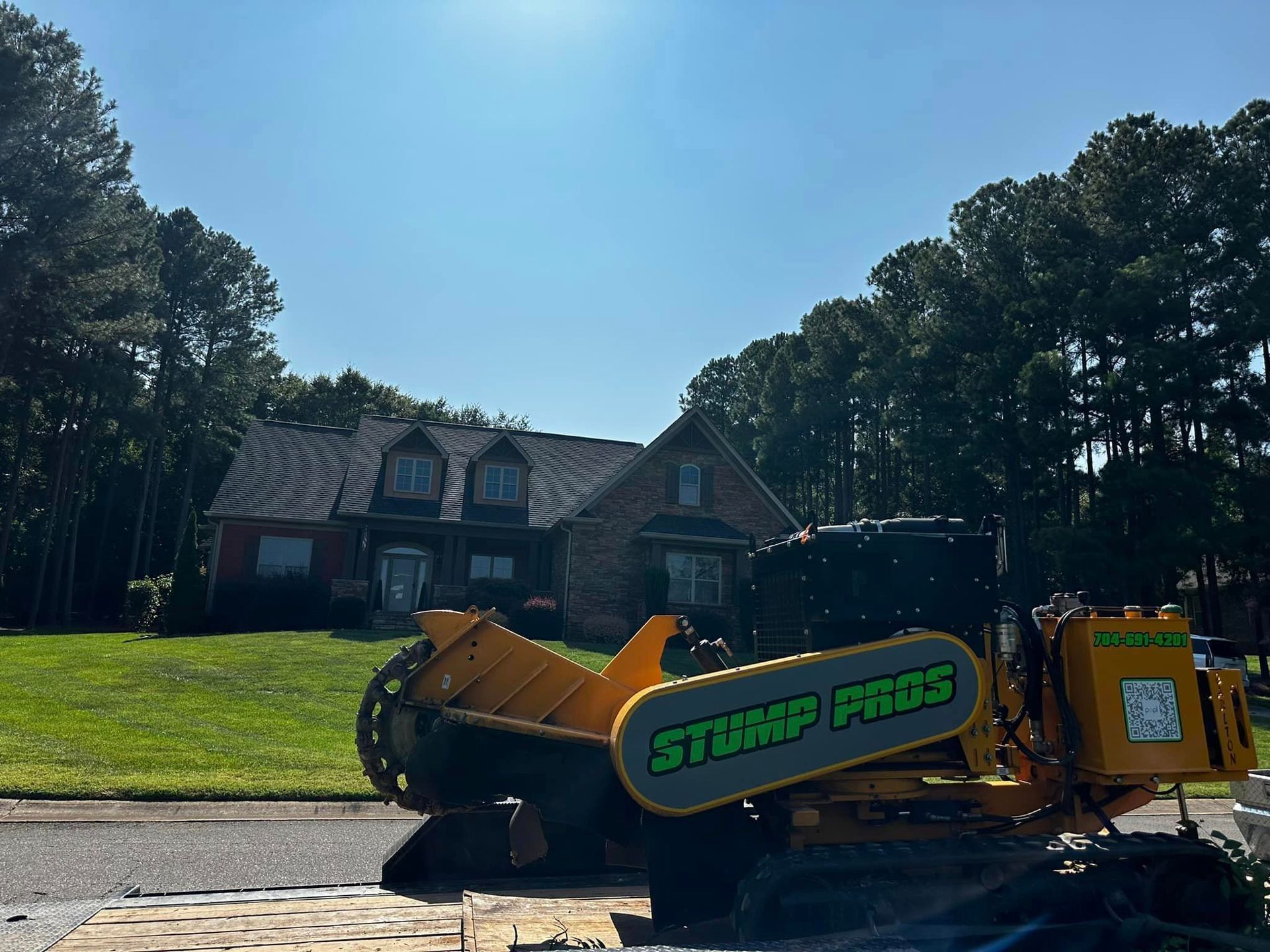 A yellow stump grinder is parked in front of a house.
