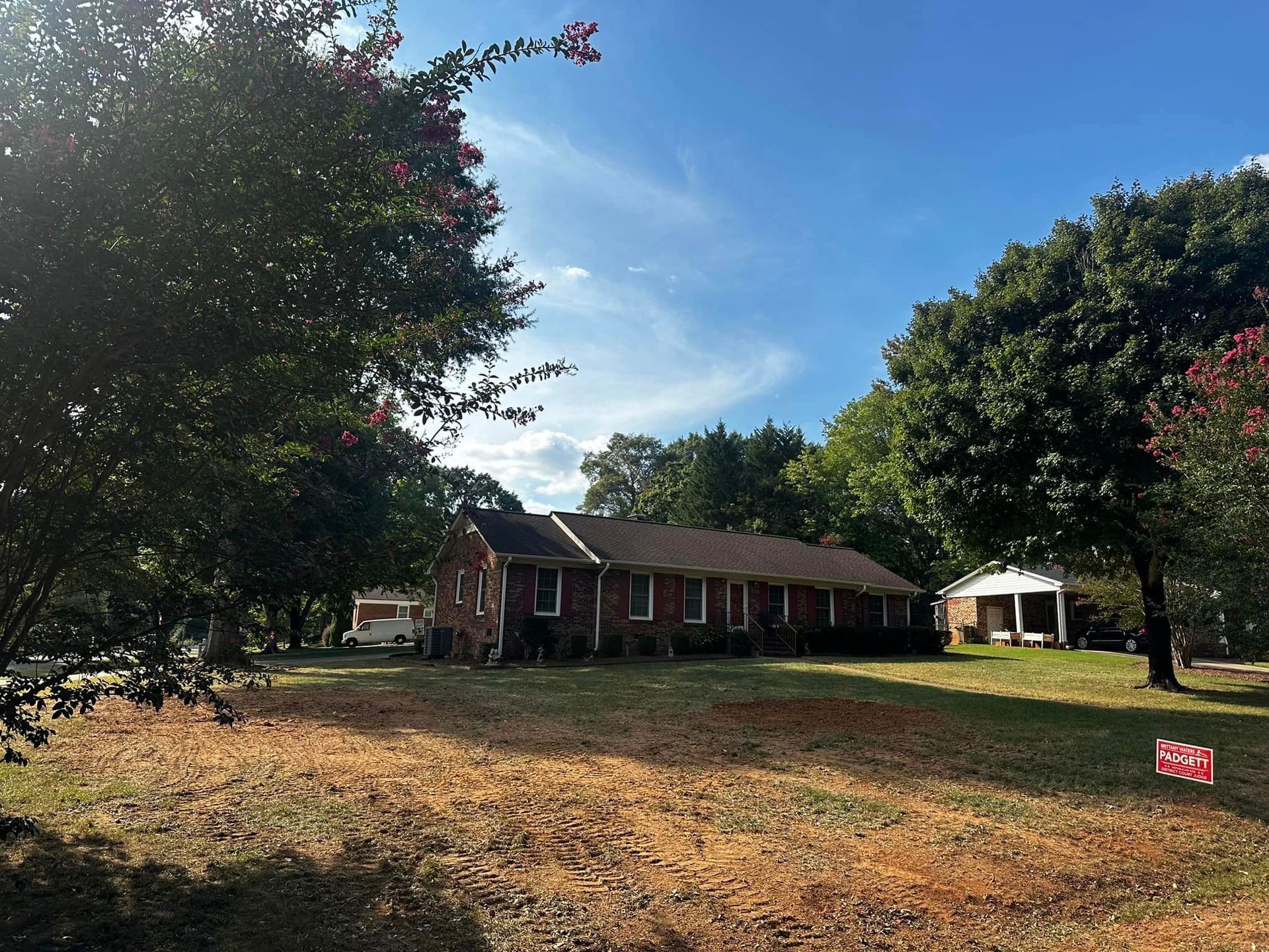 A brick house is sitting in the middle of a grassy field surrounded by trees.