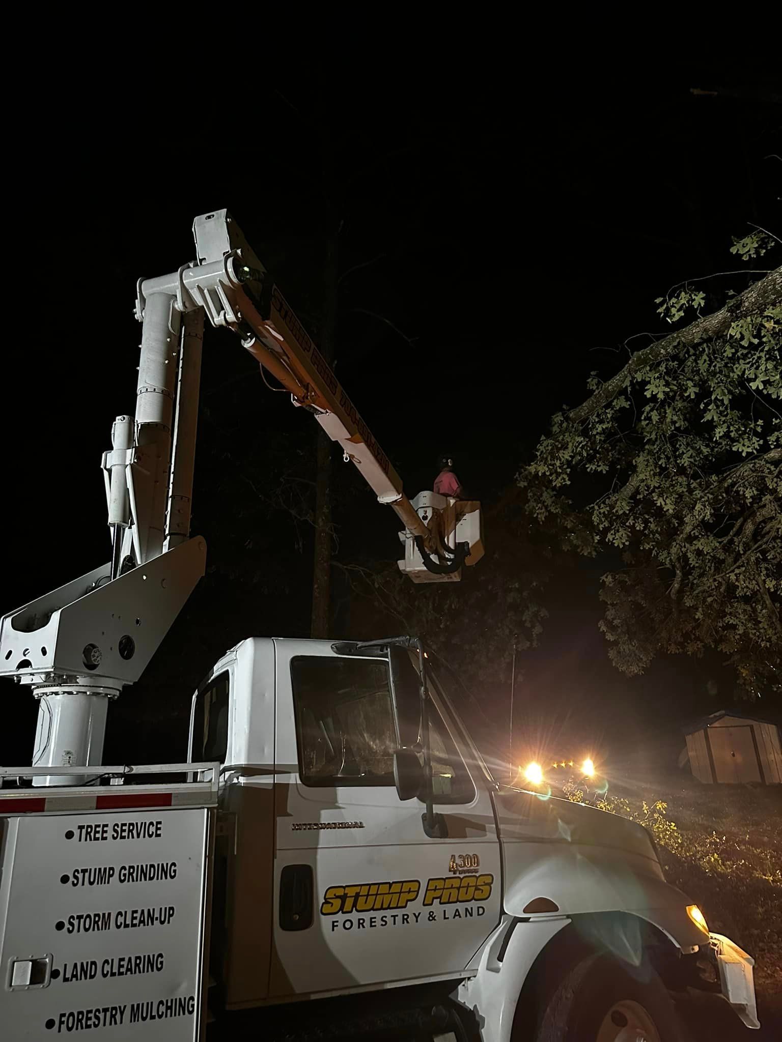 A man is sitting in a bucket on top of a truck at night.