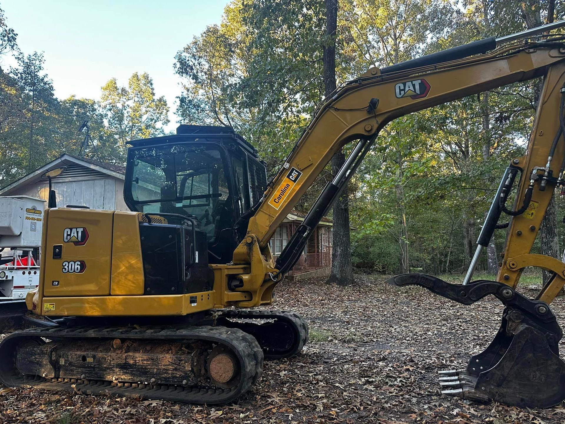 A yellow cat excavator is parked in a pile of leaves in front of a house.
