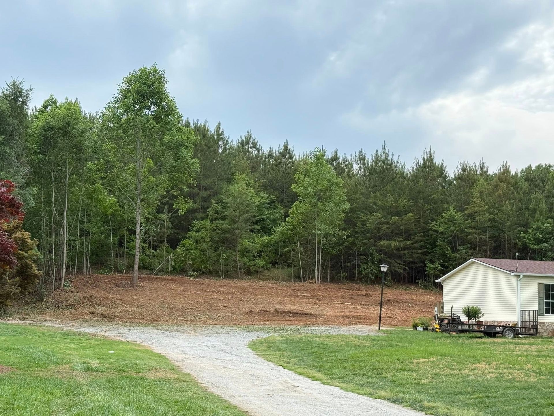 A house is sitting on top of a lush green field next to a forest.