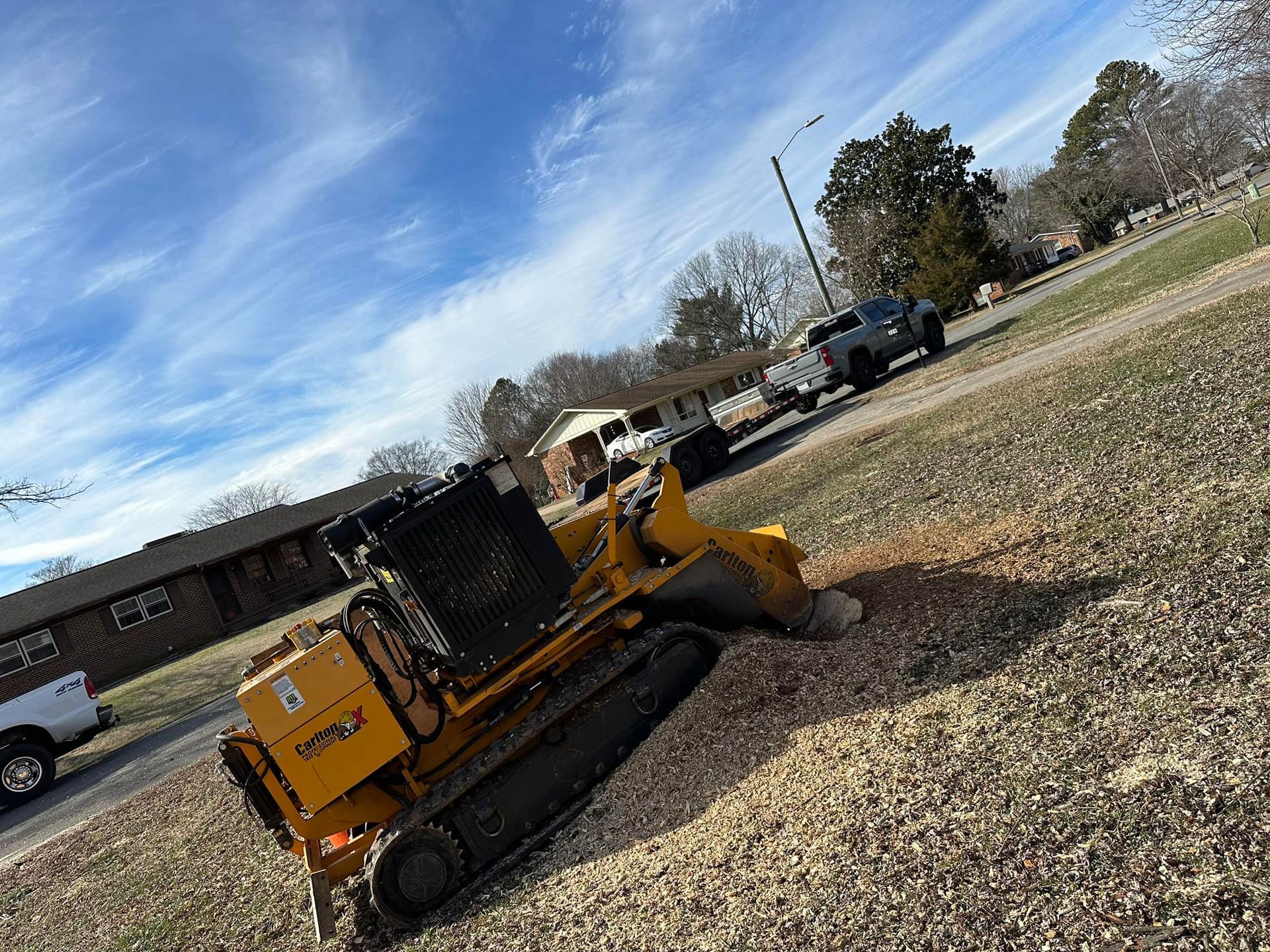 A yellow tractor is stump grinding a tree in a yard.