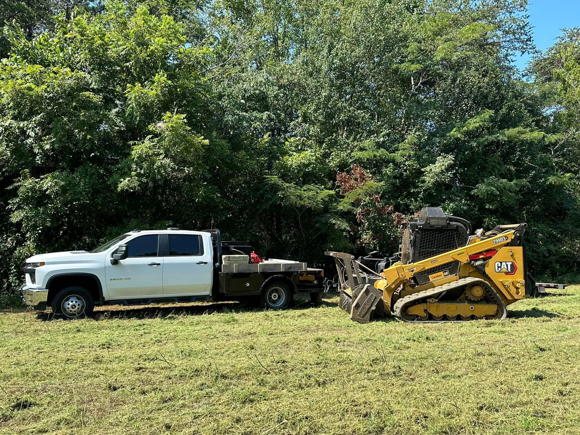 A white truck is towing a bulldozer in a grassy field.