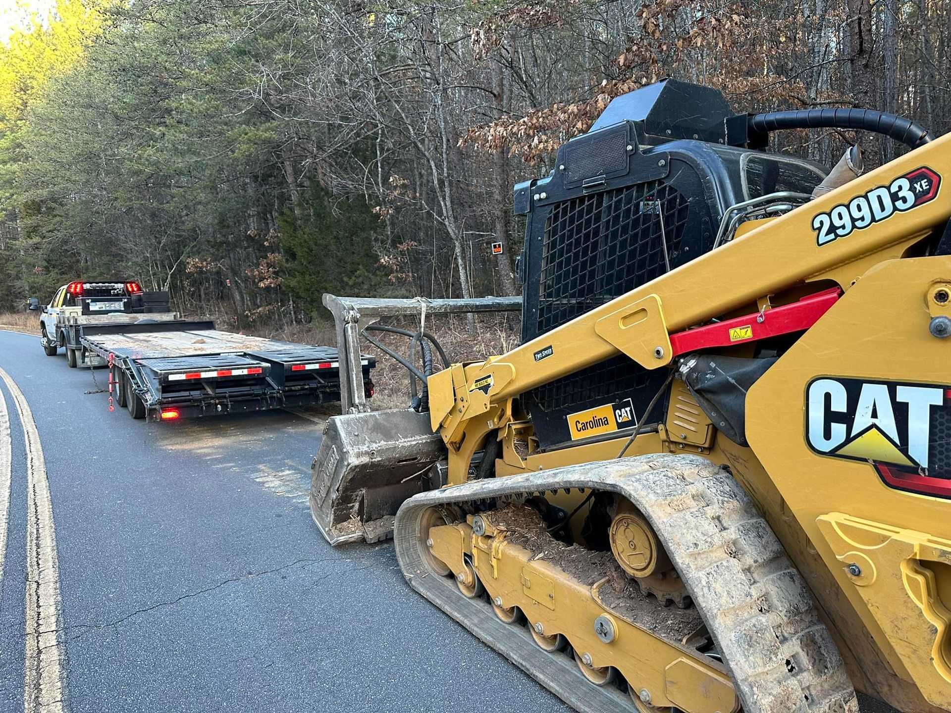 A cat bulldozer is driving down a road next to a trailer.