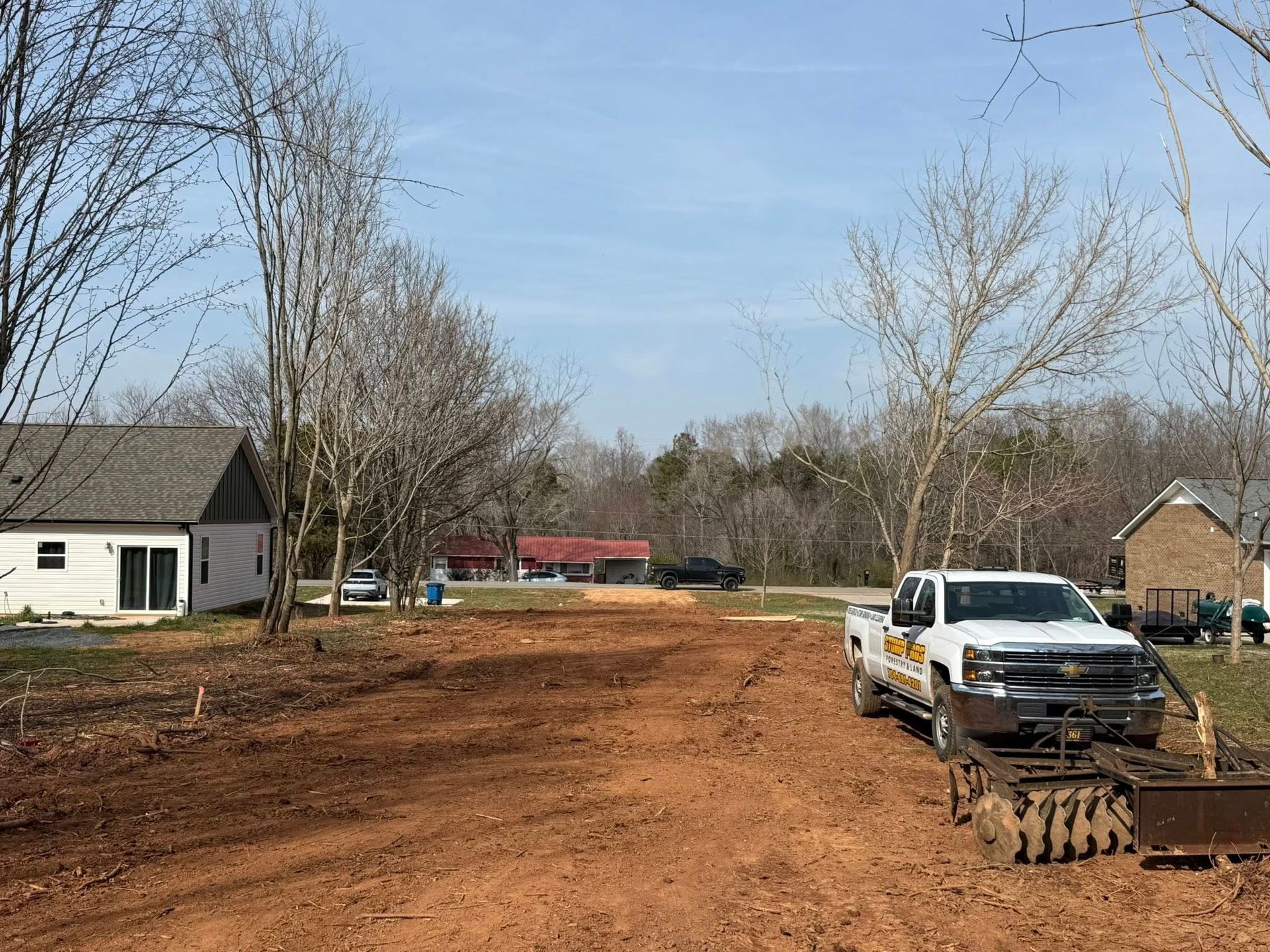 A large tree stump is sitting in the middle of a field next to a house.