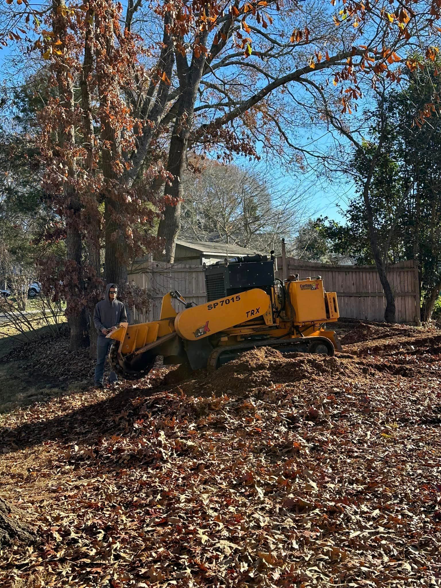 A yellow stump grinder is sitting on top of a pile of leaves in a yard.