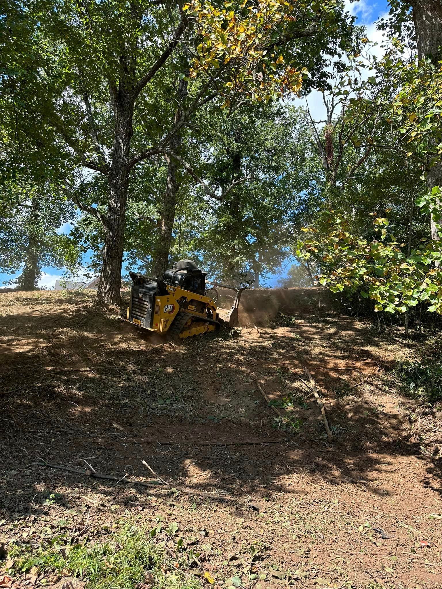 A yellow tractor is cutting a tree in the woods.