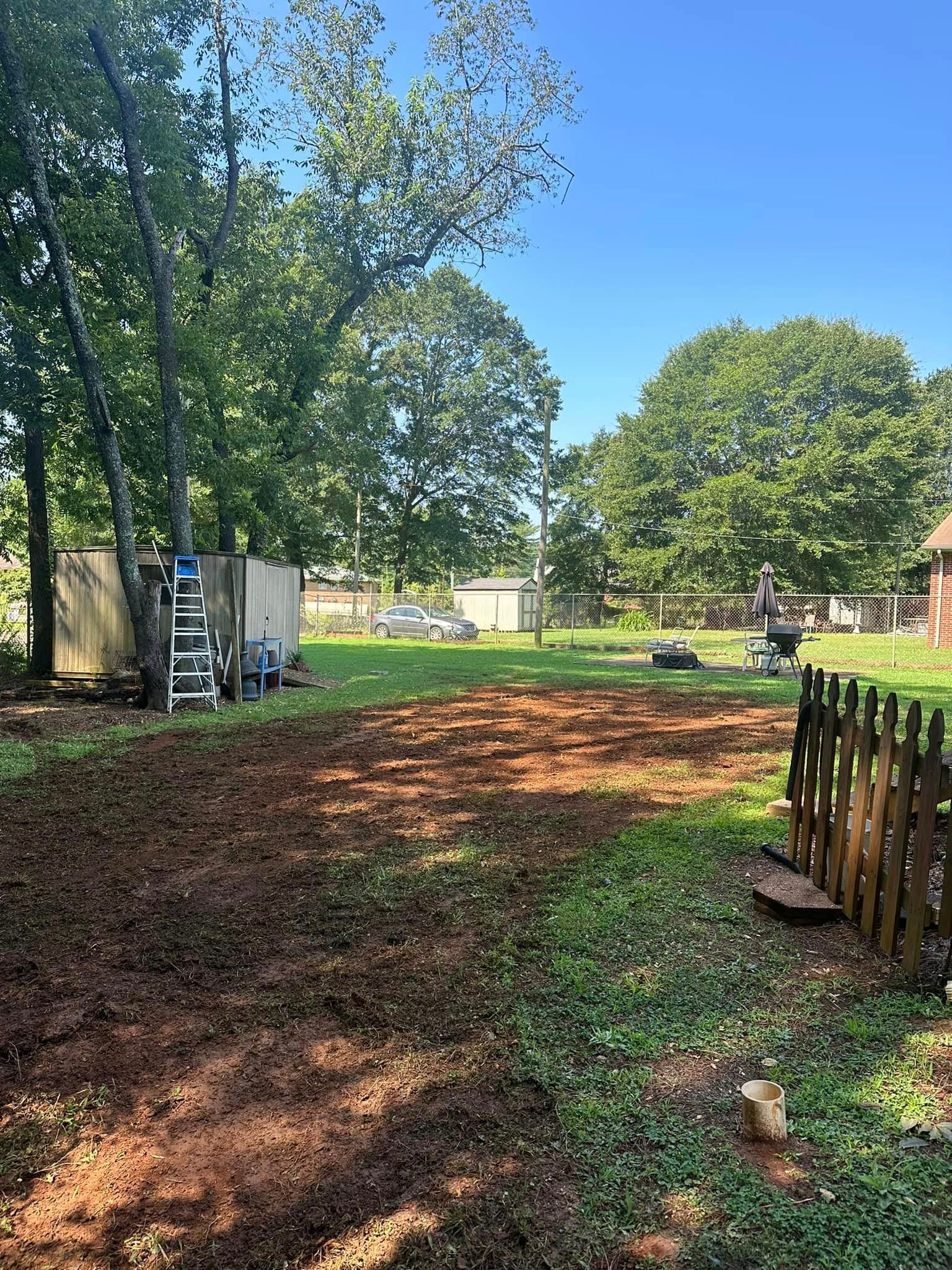 A large yard with a wooden fence and trees in the background.
