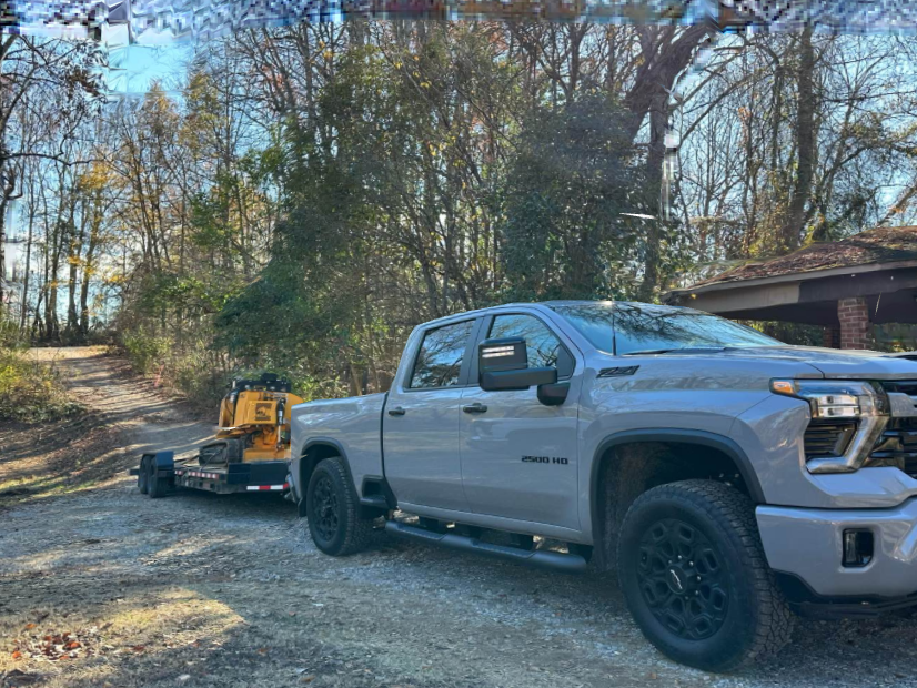 A gray truck is towing a yellow trailer down a dirt road.