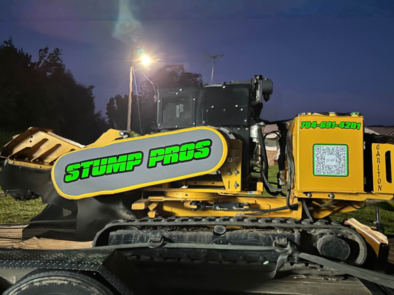 A yellow stump pros tractor is parked on a trailer