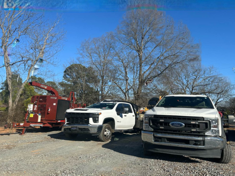 Two white trucks are parked next to each other in a gravel lot.