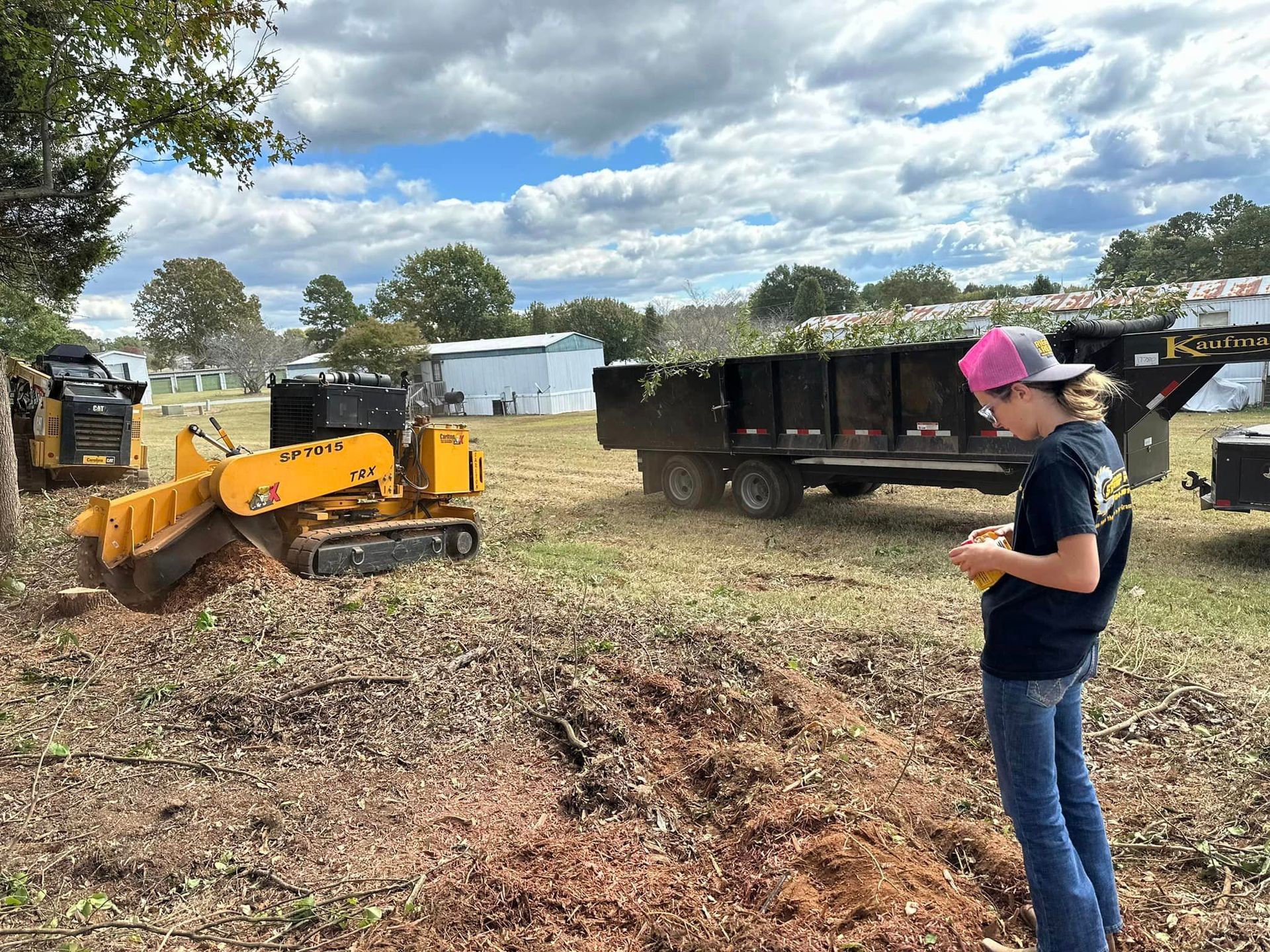 A woman is standing in a field looking at a stump grinder.