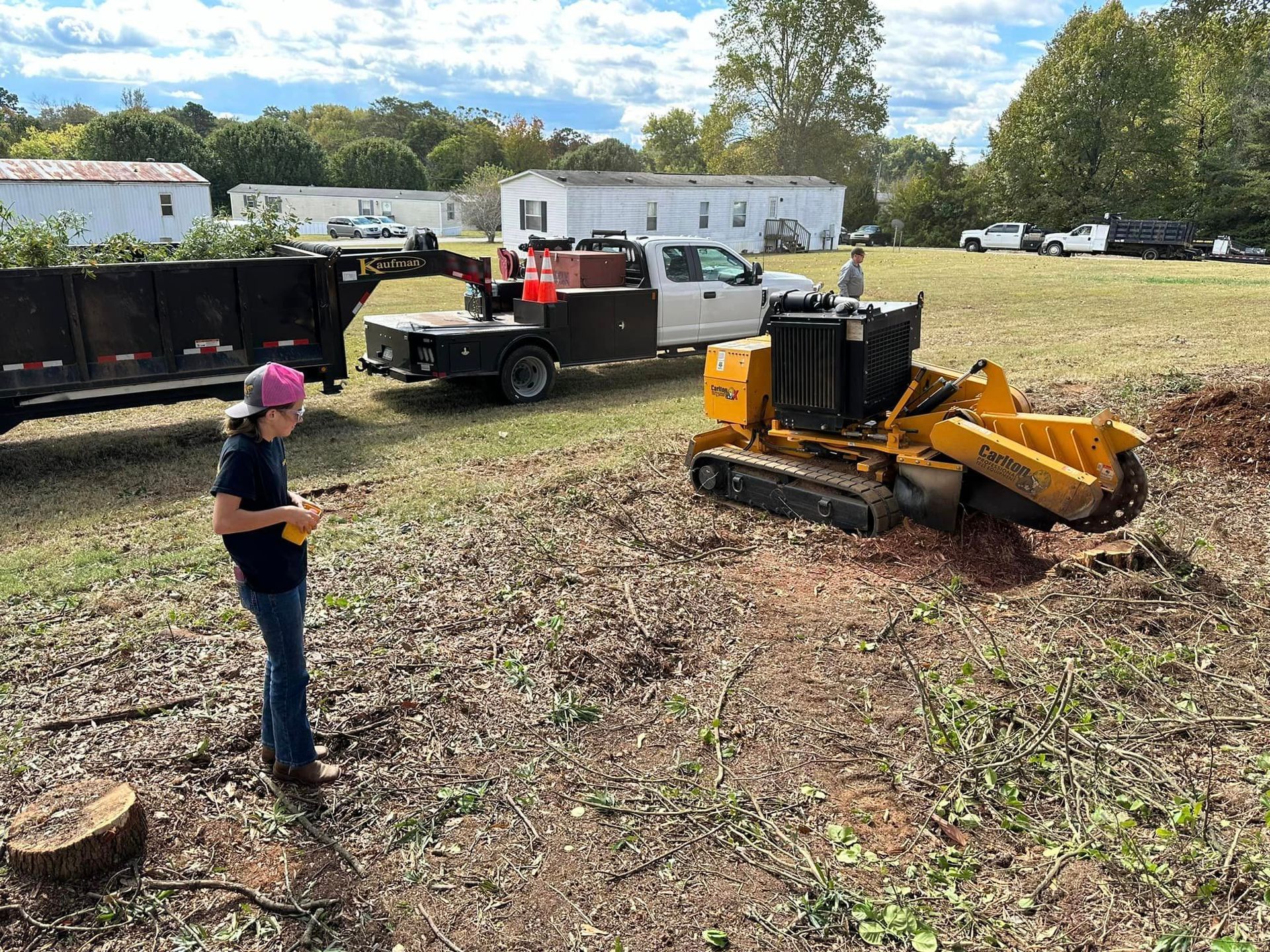 A woman is standing next to a stump grinder in a field.