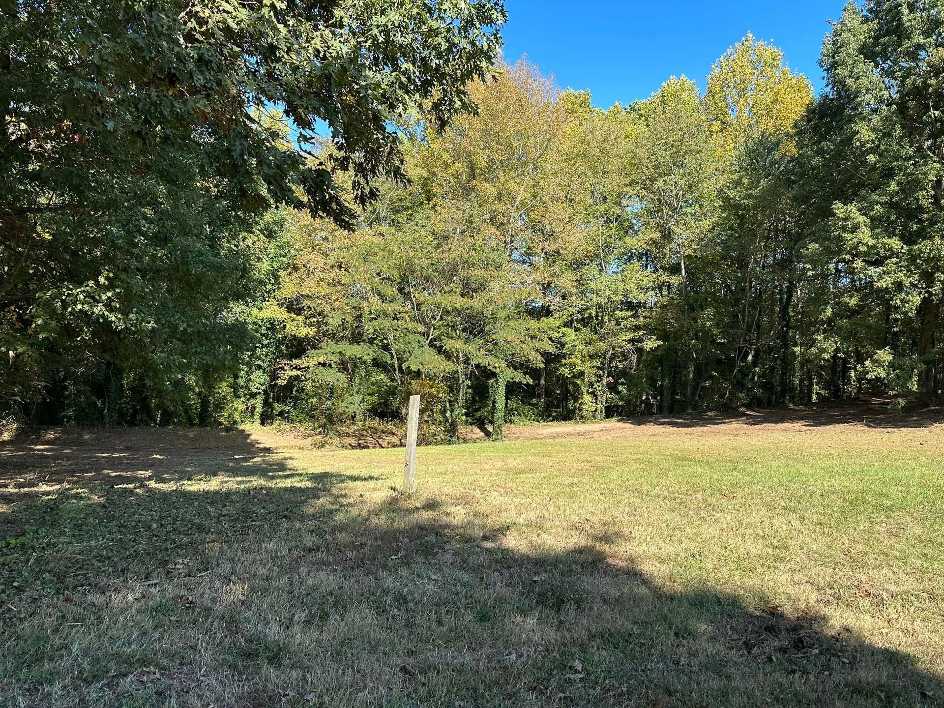 A field with trees in the background and a white pole in the middle of it.