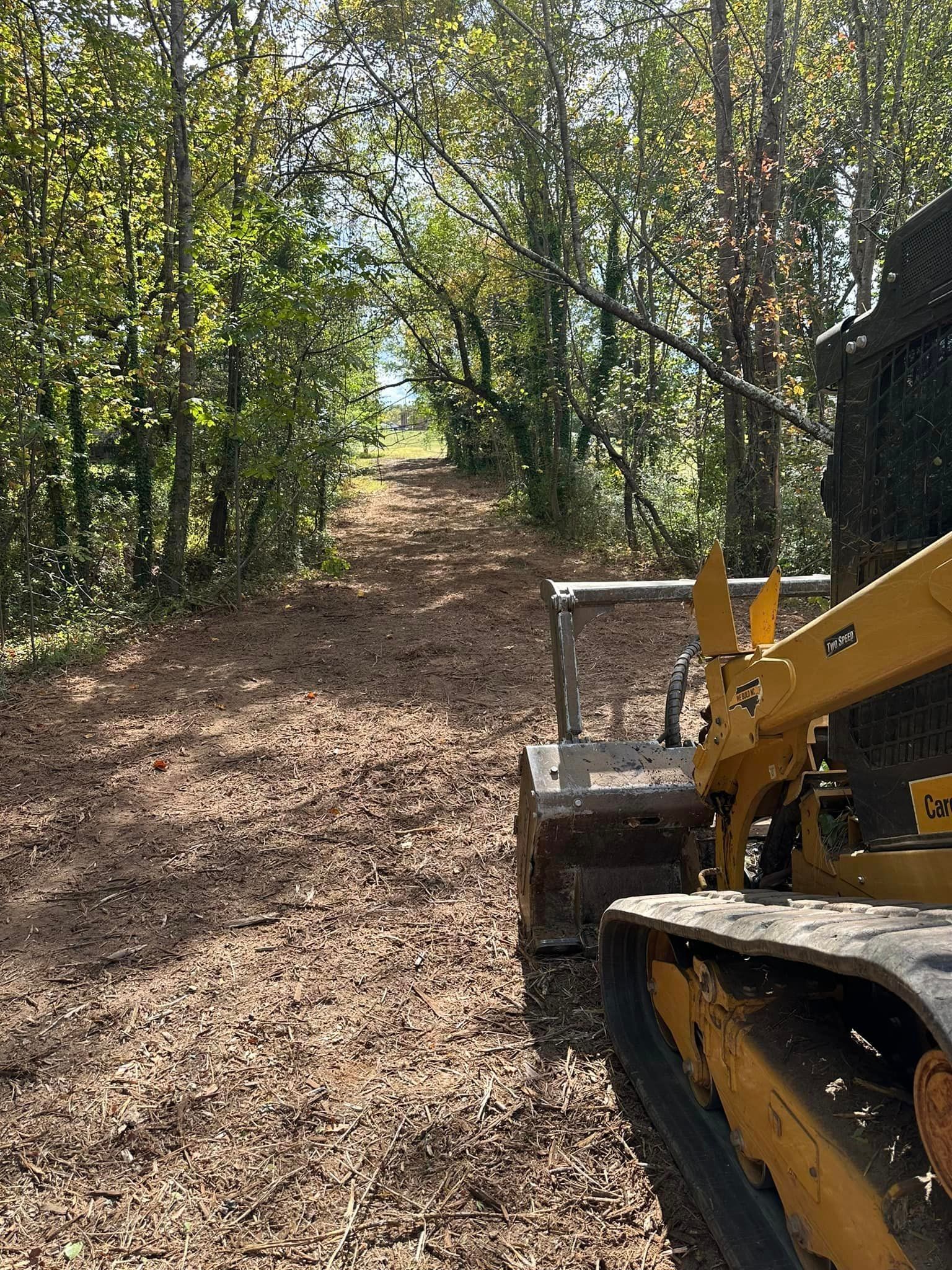 A bulldozer is driving down a dirt road in the woods.