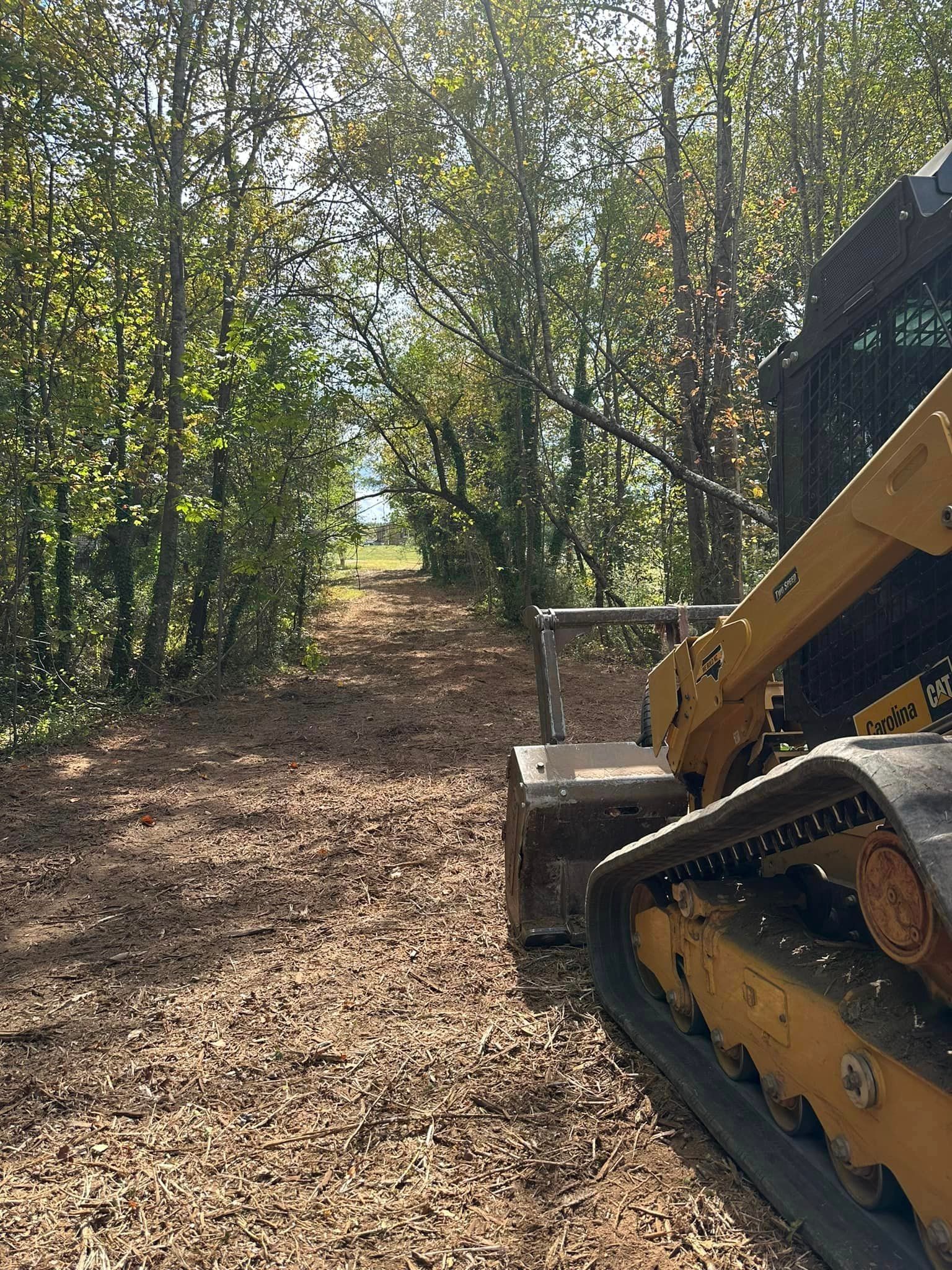 A bulldozer is driving down a dirt road in the woods.