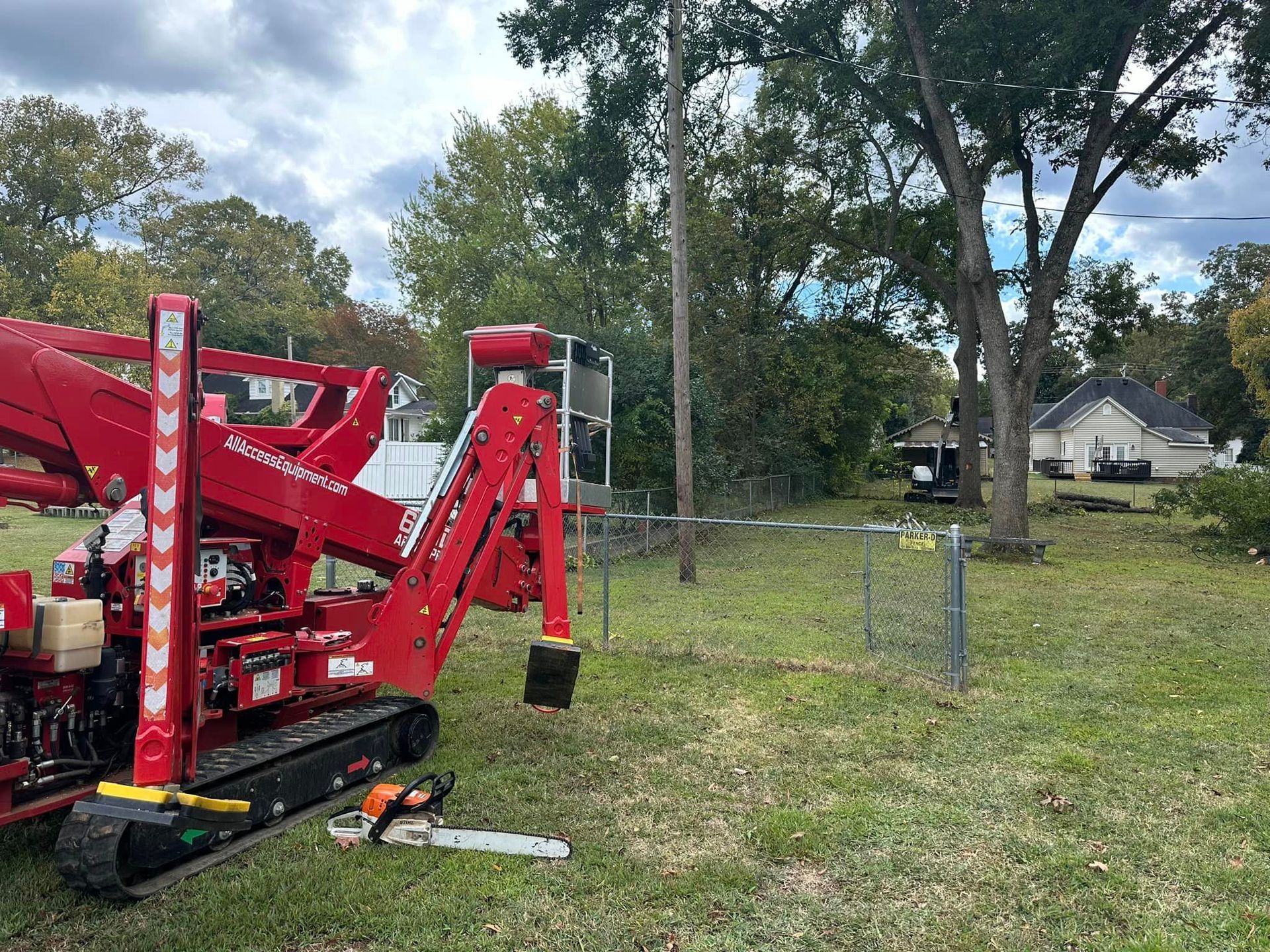 A red crane is parked in a grassy field next to a chainsaw.