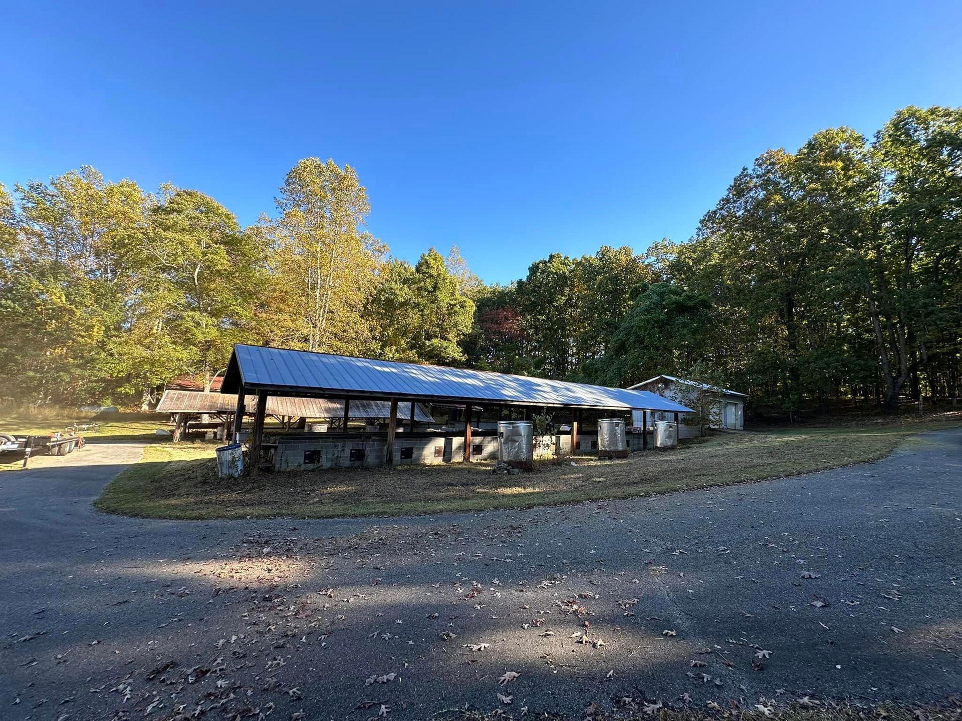 A large building with a metal roof is surrounded by trees on a sunny day.