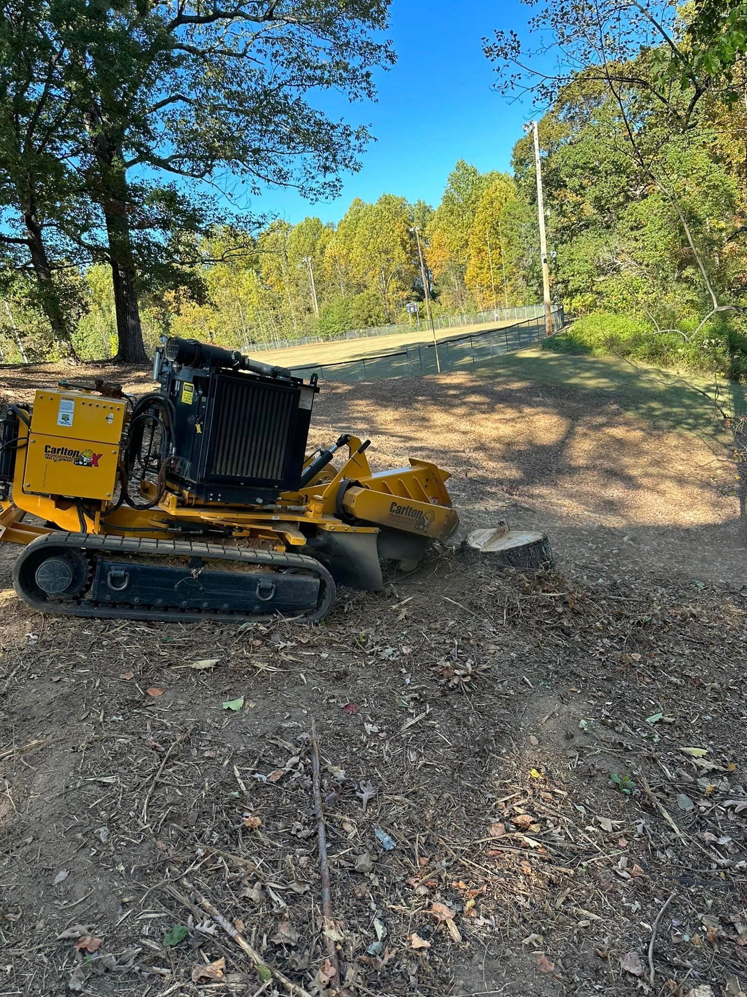 A yellow stump grinder is sitting in the middle of a dirt field.