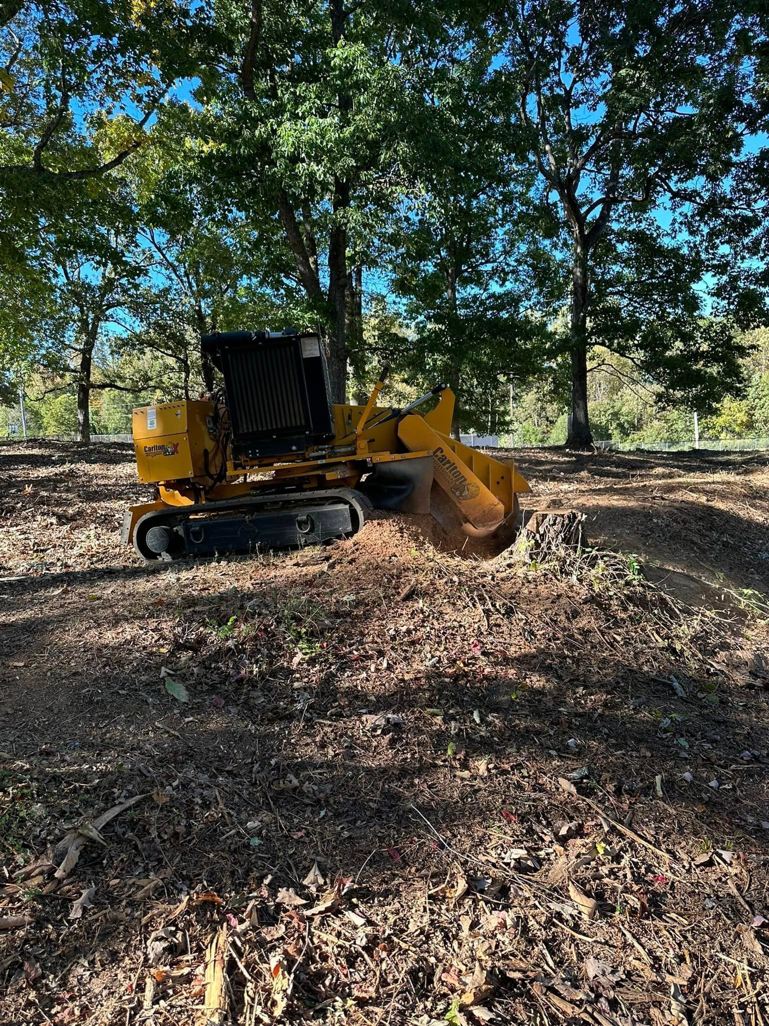 A yellow stump grinder is sitting in the middle of a forest.
