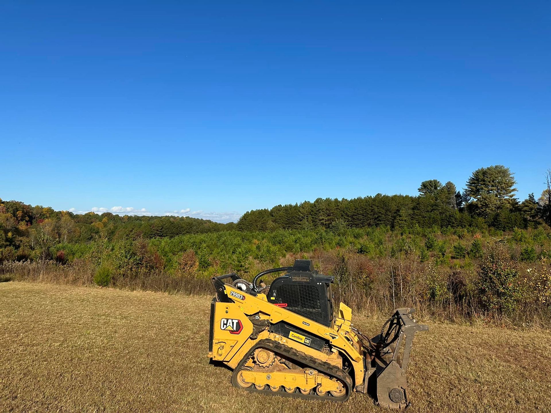 A yellow bulldozer is parked in a field with trees in the background.