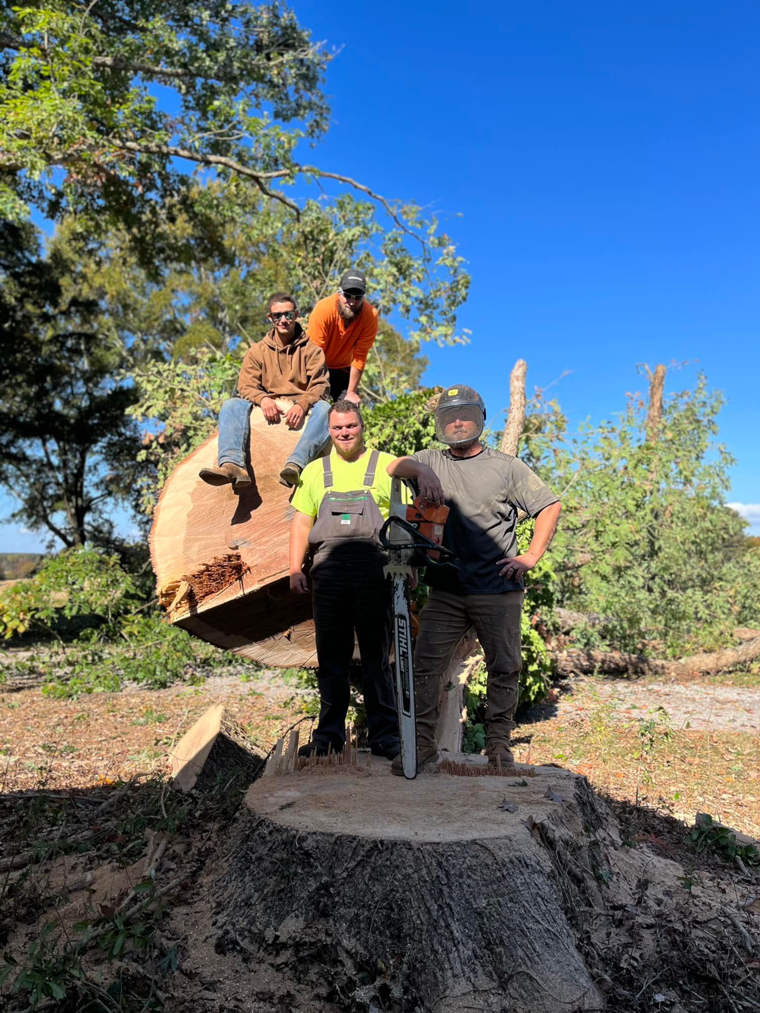 A group of men are standing around a tree stump with a chainsaw.