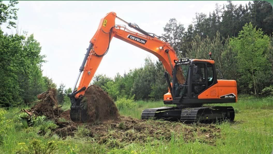 A large orange excavator is digging a hole in a grassy field.