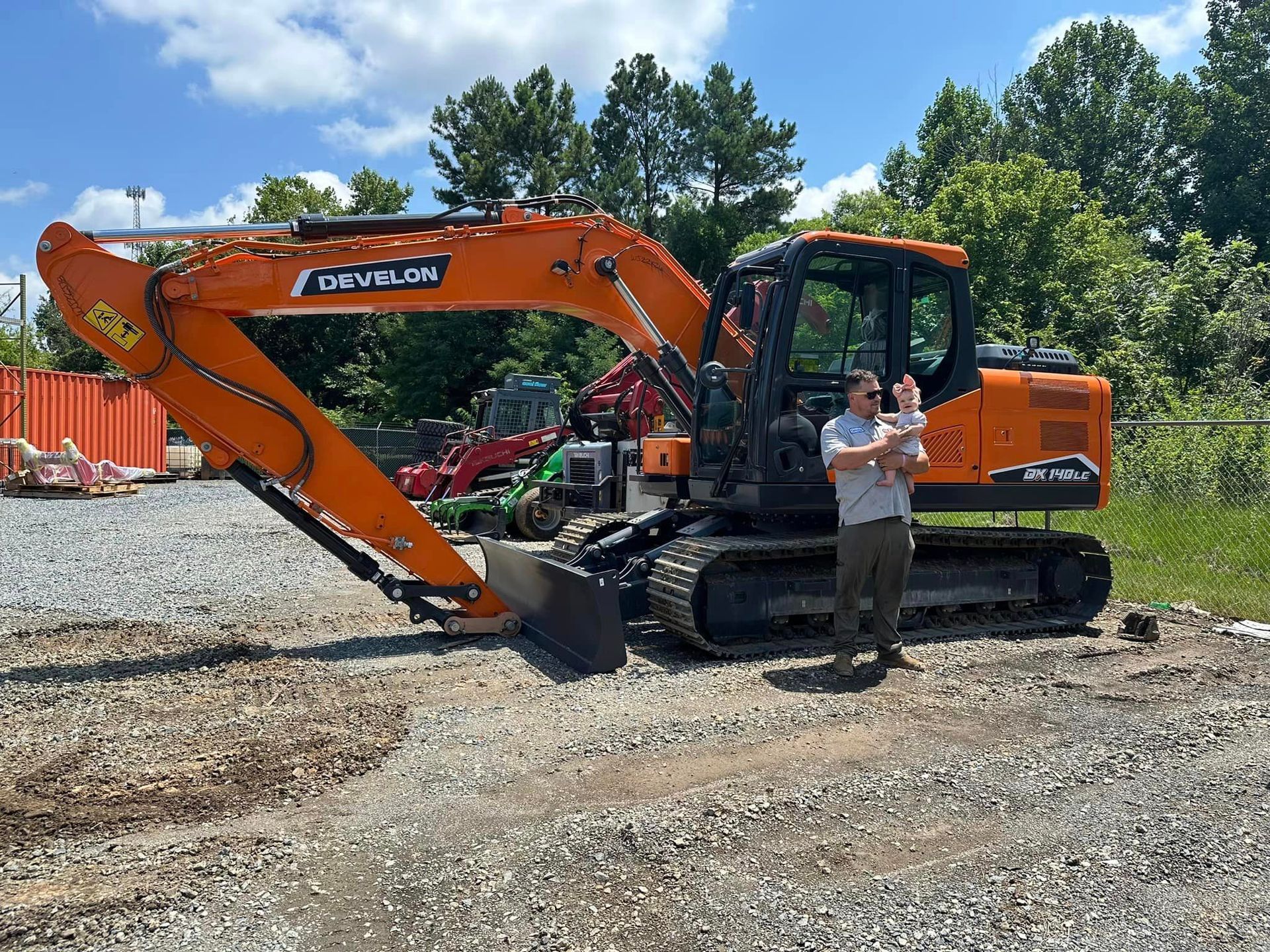 A man is standing in front of a large orange excavator.