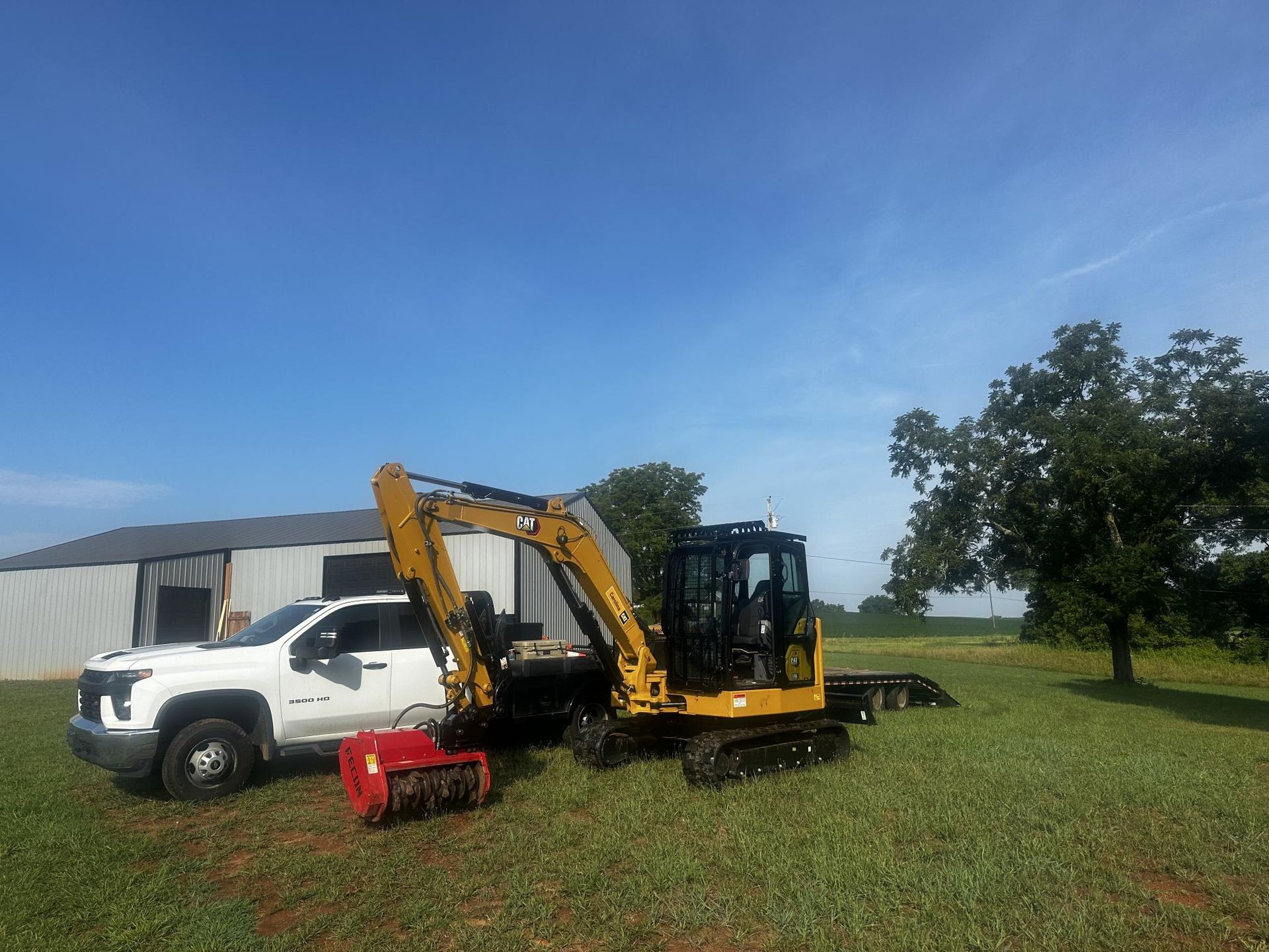 A white truck is parked next to a yellow excavator in a grassy field.