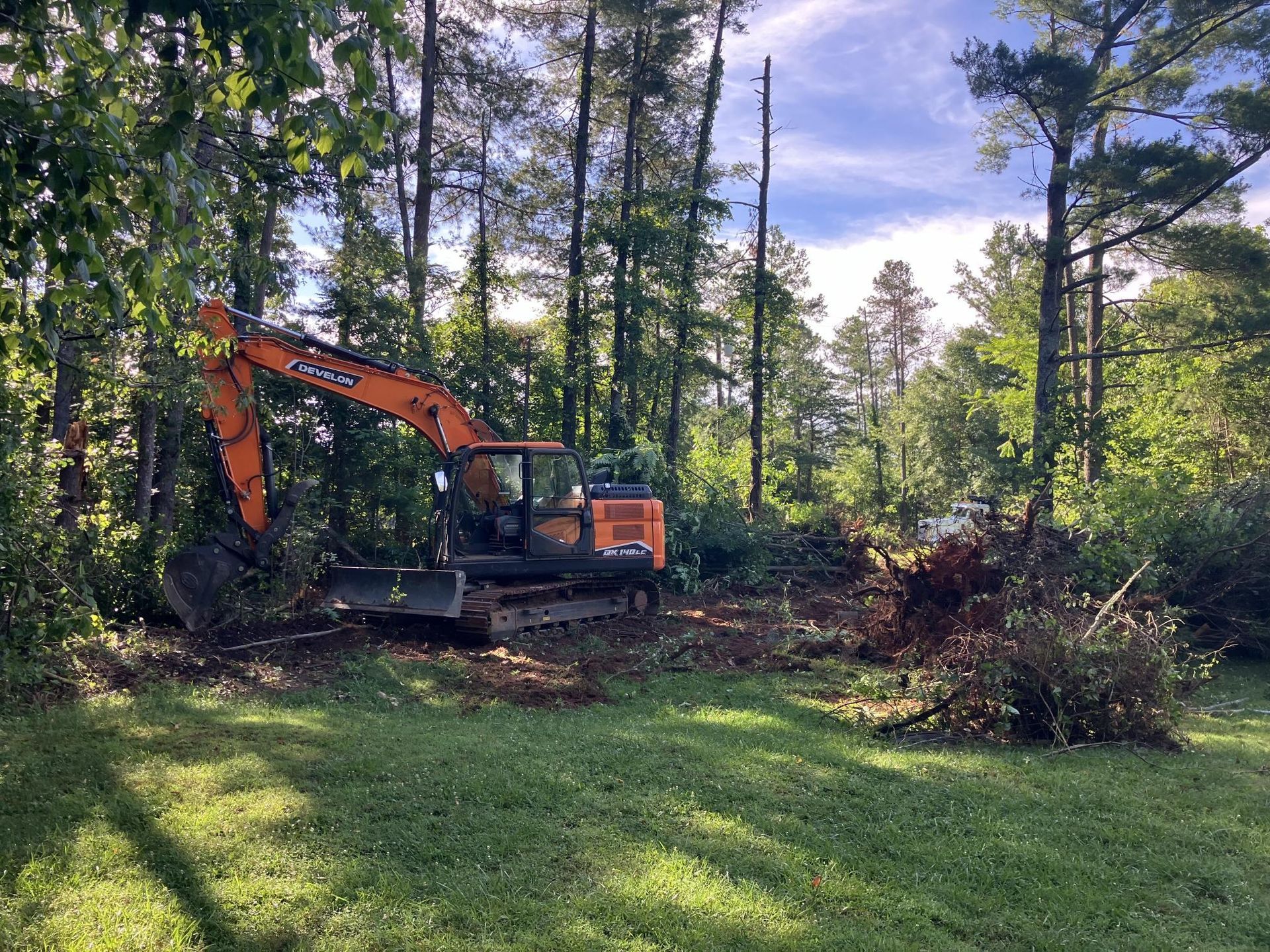 A large orange excavator is sitting in the middle of a lush green field.
