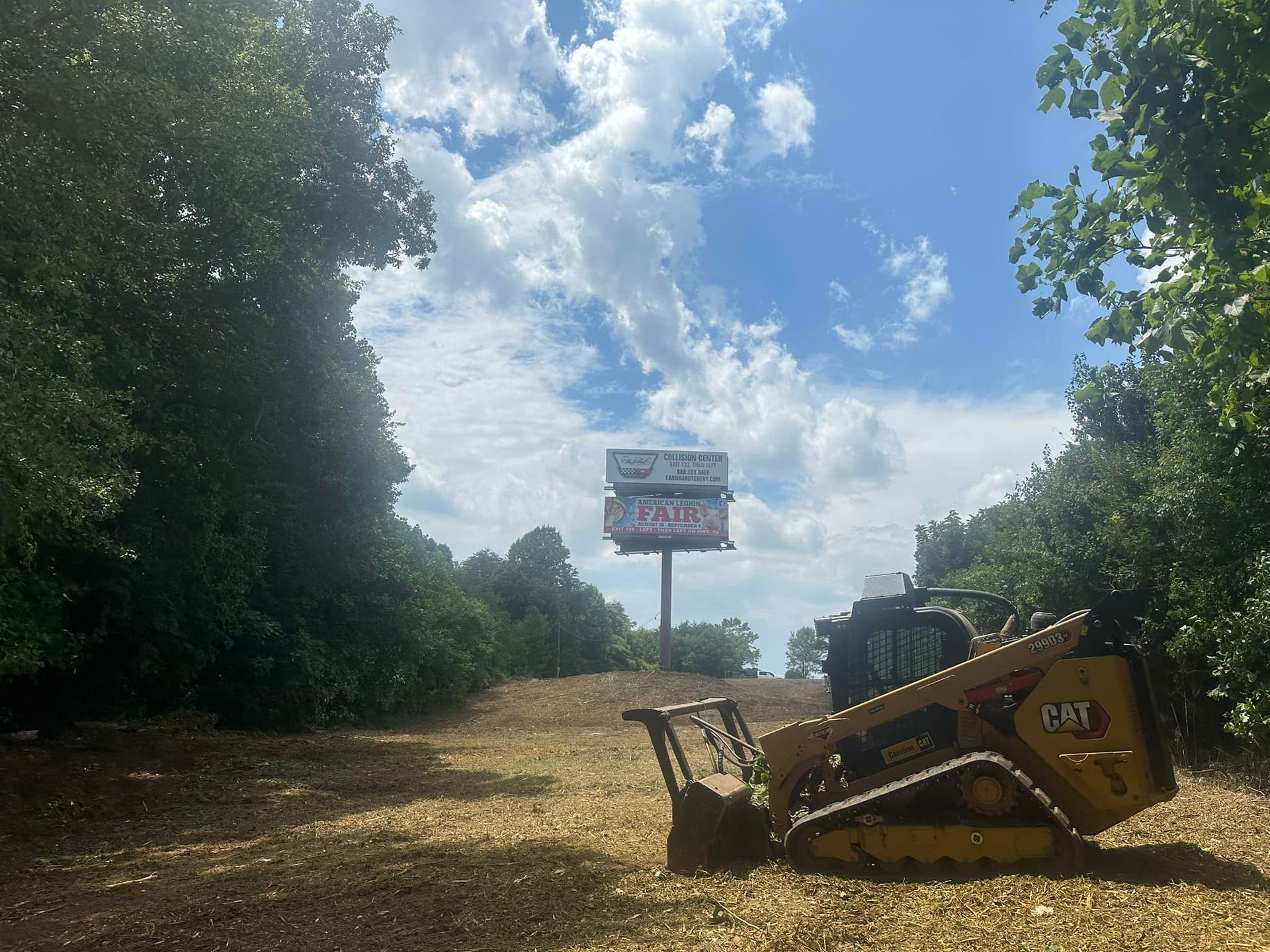 A bulldozer is driving down a dirt road next to a billboard.