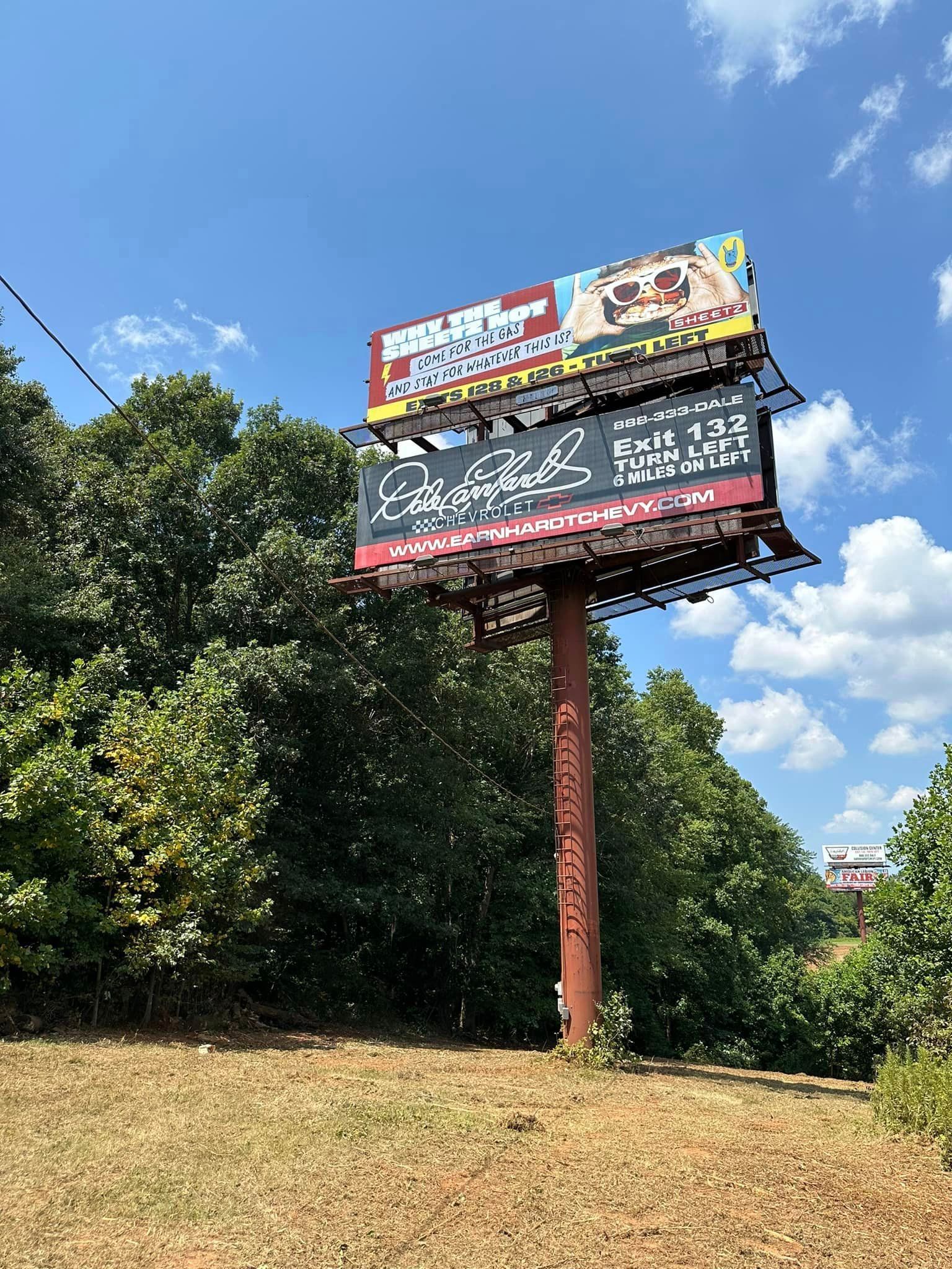 A large billboard is sitting in the middle of a field surrounded by trees.