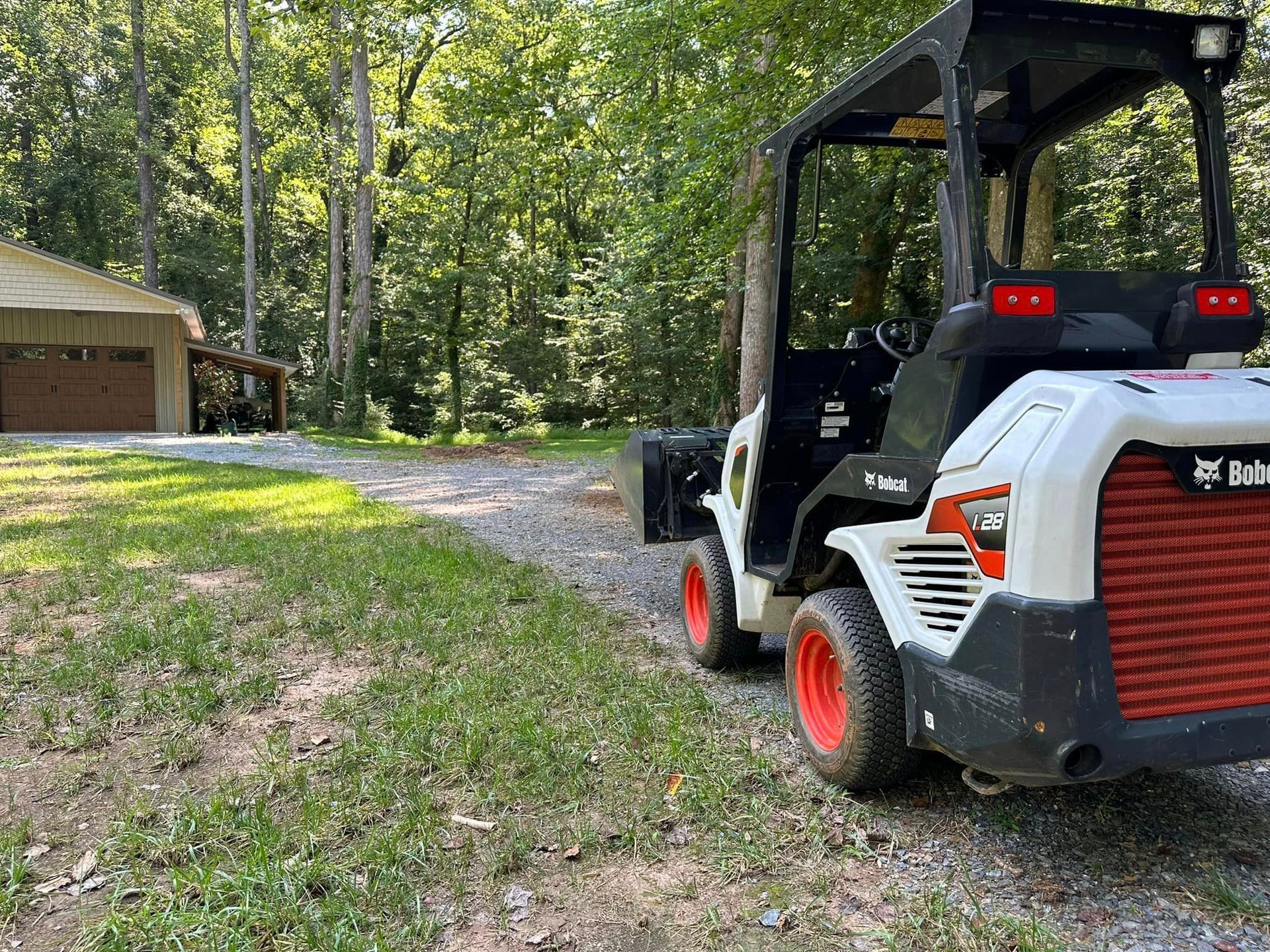 A bobcat tractor is parked in a driveway next to a garage.