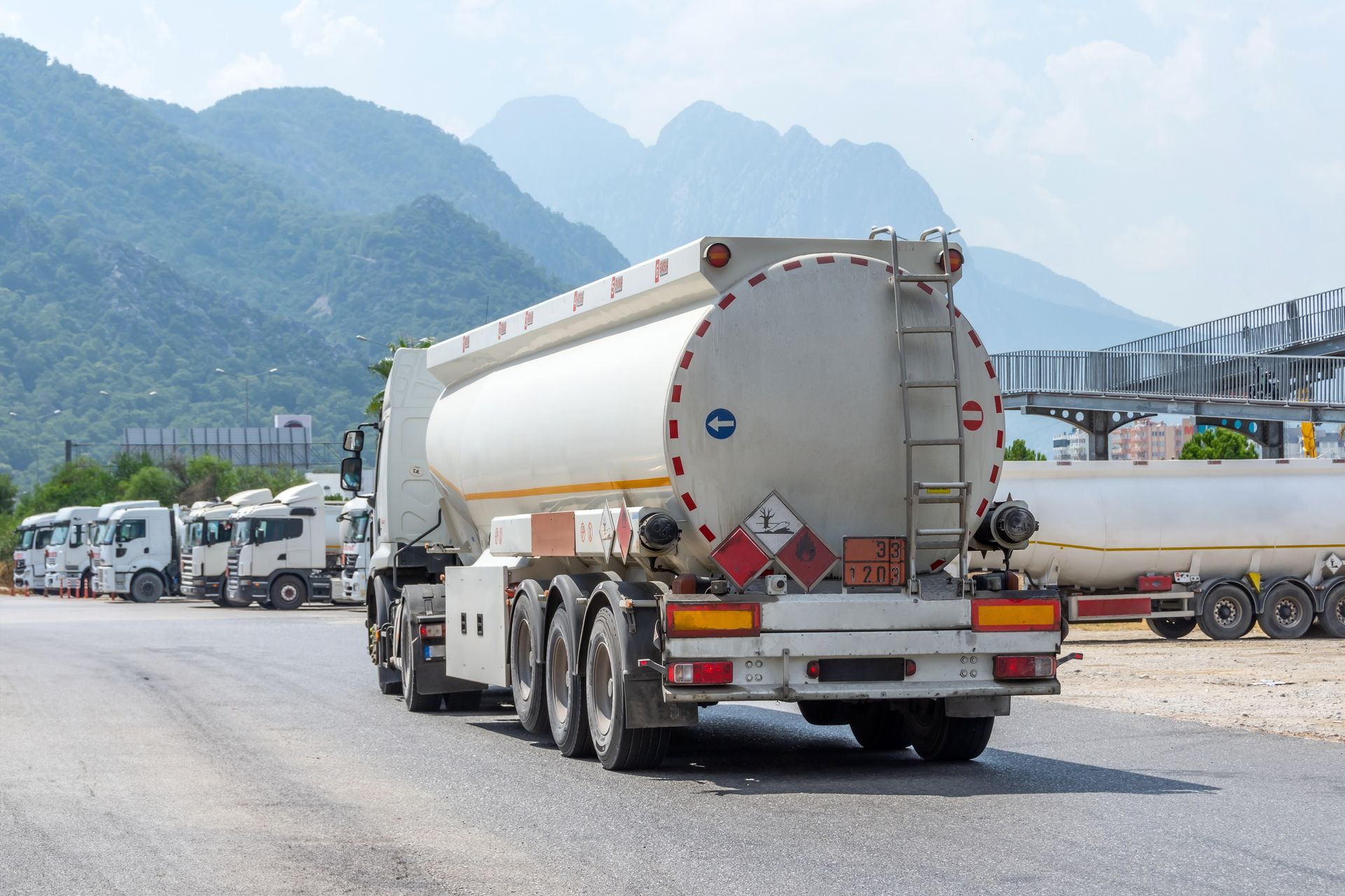 A tanker truck is driving down a road with mountains in the background.