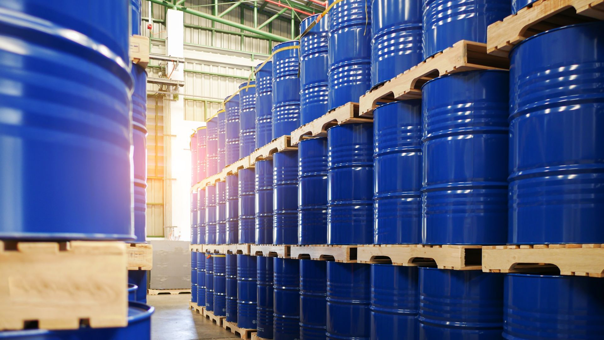 A warehouse filled with lots of blue barrels on wooden pallets.