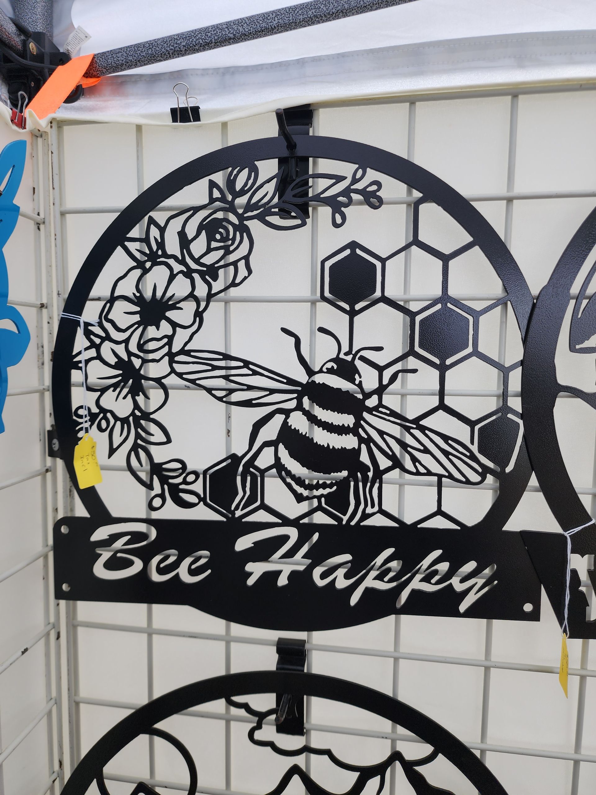 Black metal art sign with a bee, honeycomb, and flowers, reading 