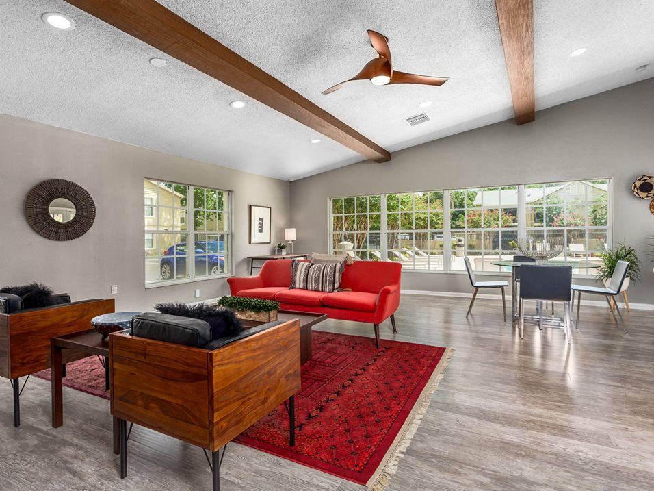 Living room with red sofa, rug, and wooden beams, large windows, and modern furniture.