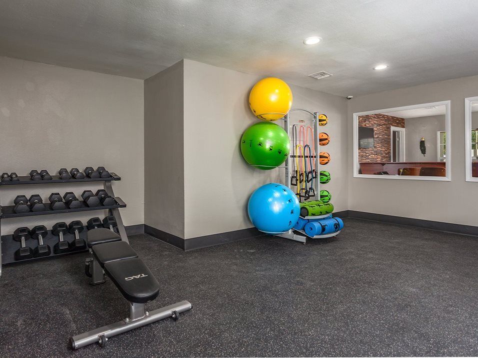 Gym with weights, bench, exercise balls, and equipment rack on black rubber flooring.