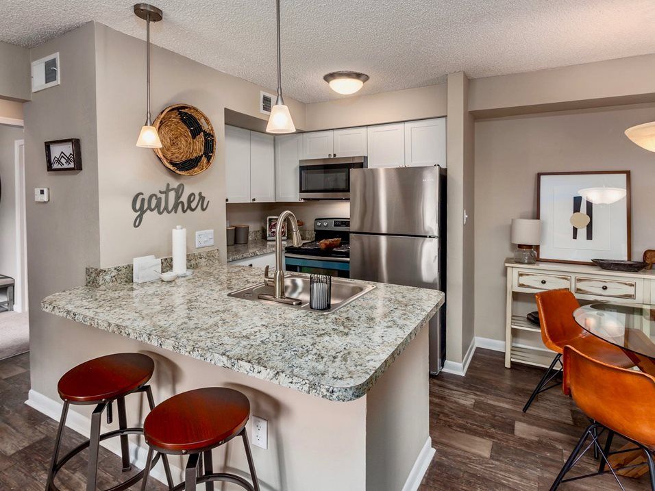 Kitchen with granite countertop island, stainless steel appliances, stools, and 'gather' sign.